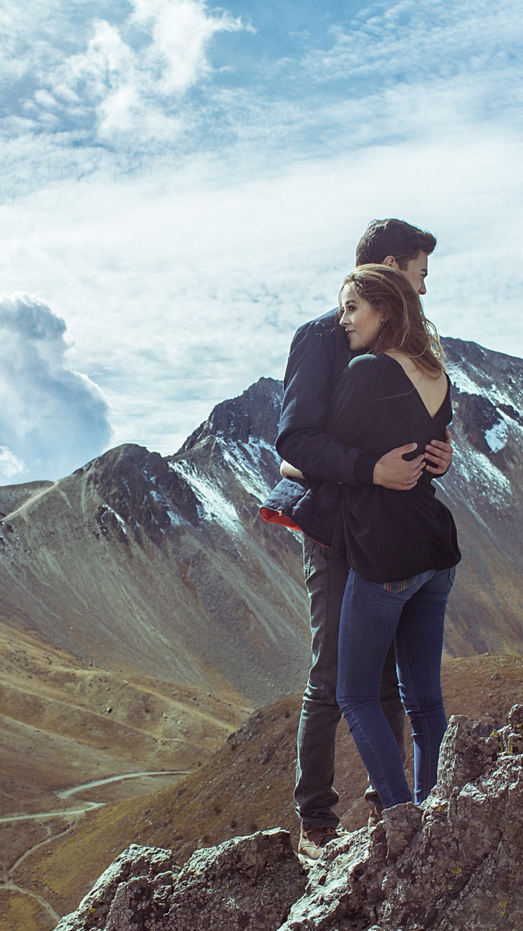 Hombre de Chaqueta Negra y Pantalón Negro de Pie Sobre la Formación Rocosa Bajo Las Nubes Blancas Durante el Día. Wallpaper in 750x1334 Resolution
