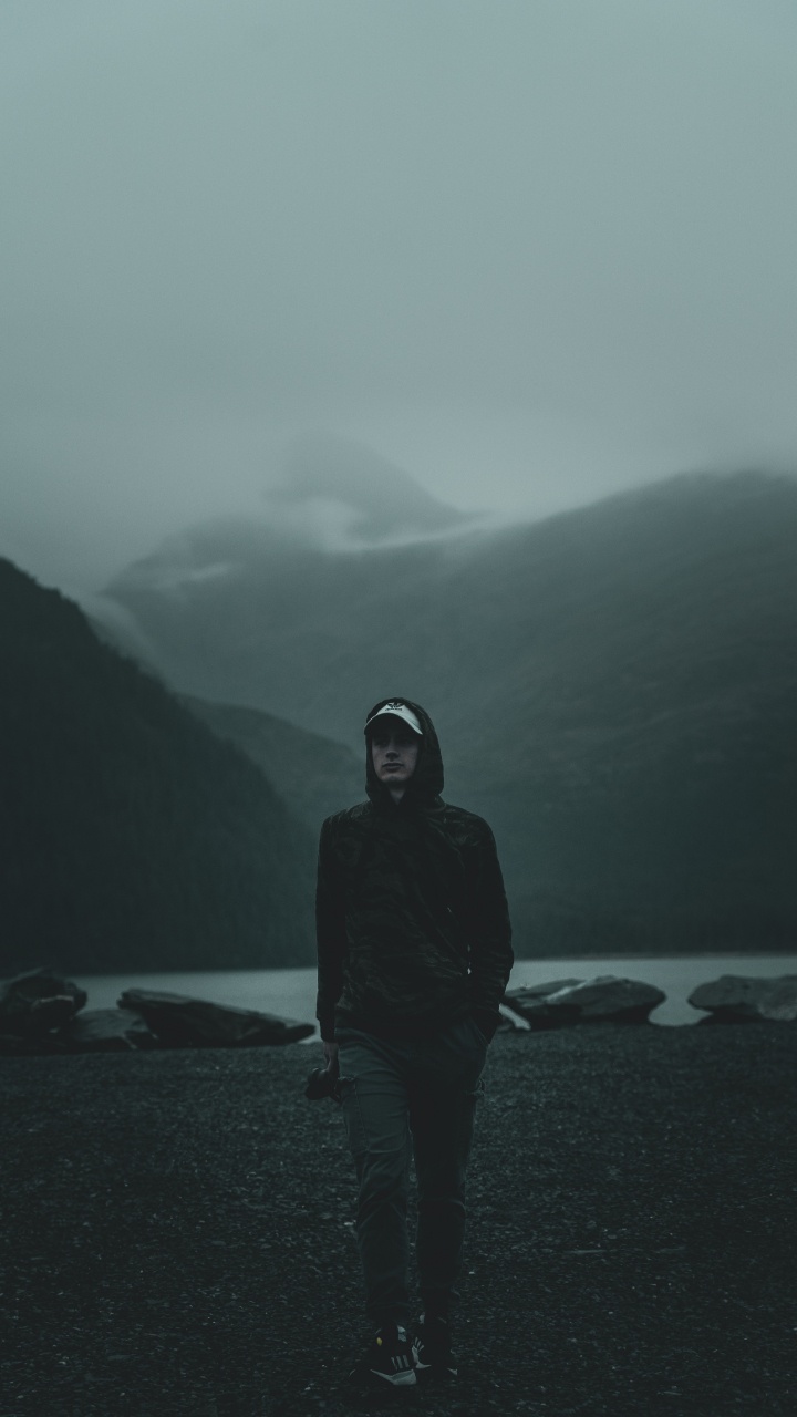 Man in Black Hoodie Debout Sur la Plage Pendant la Journée. Wallpaper in 720x1280 Resolution