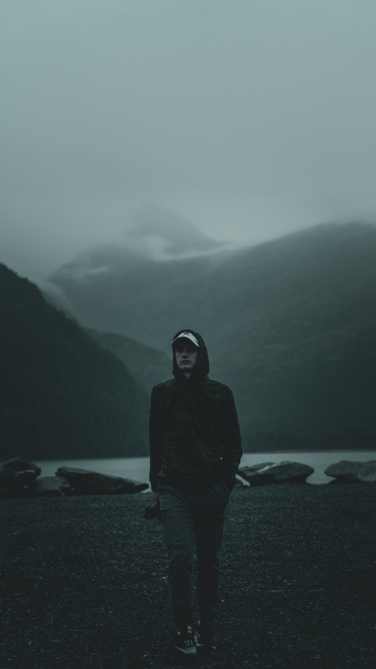 Man in Black Hoodie Standing on Beach During Daytime. Wallpaper in 750x1334 Resolution