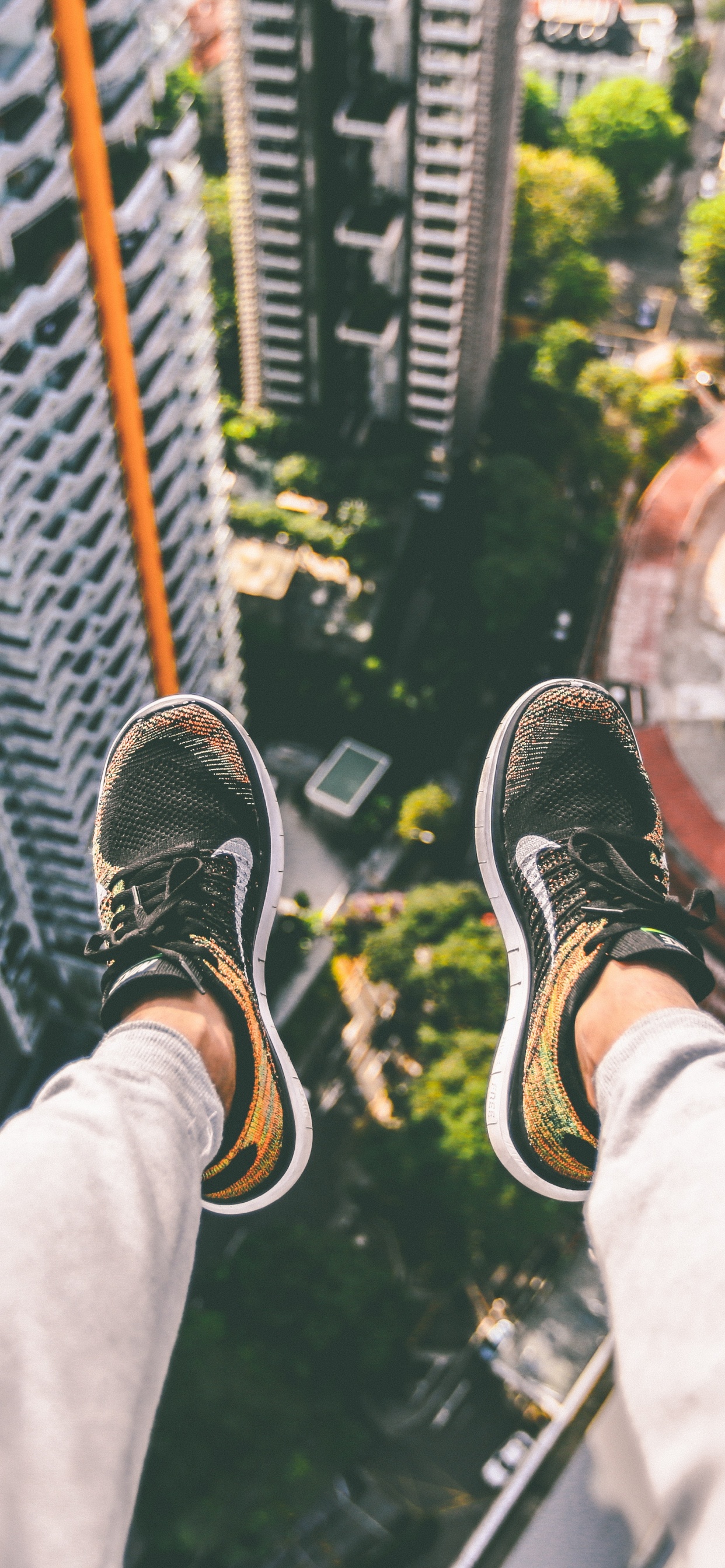 Person in Black and White Sneakers Sitting on Top of Building. Wallpaper in 1242x2688 Resolution