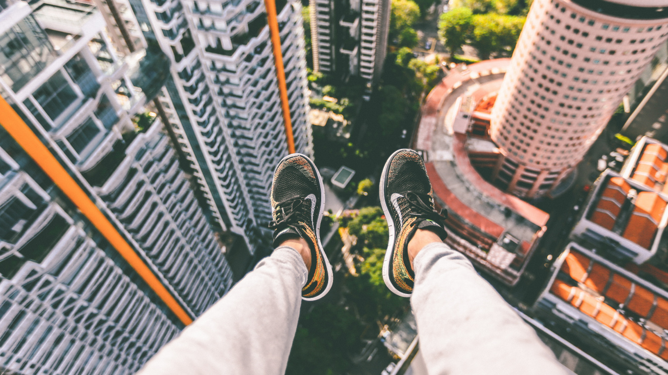 Person in Black and White Sneakers Sitting on Top of Building. Wallpaper in 1366x768 Resolution