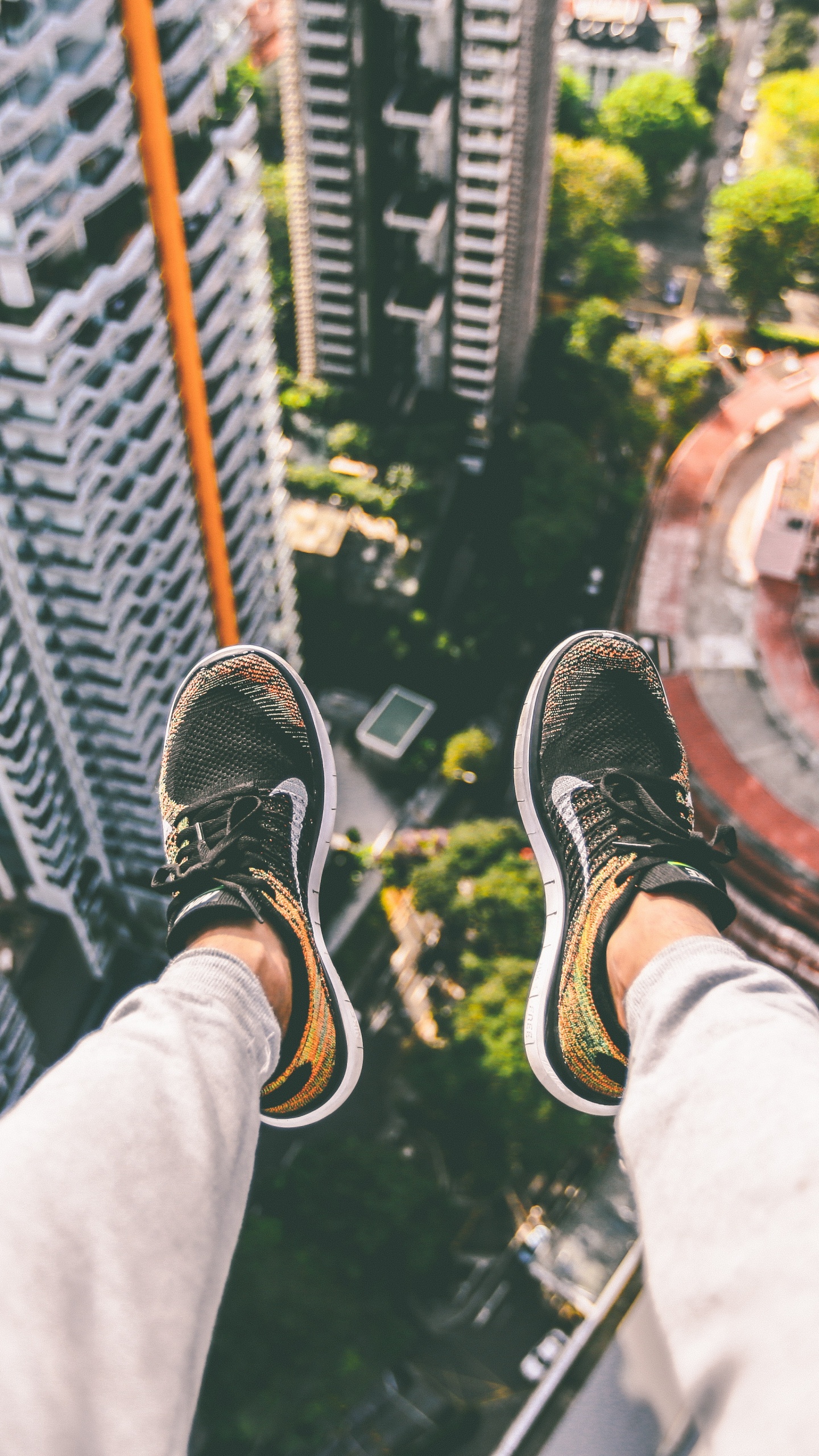 Person in Black and White Sneakers Sitting on Top of Building. Wallpaper in 1440x2560 Resolution