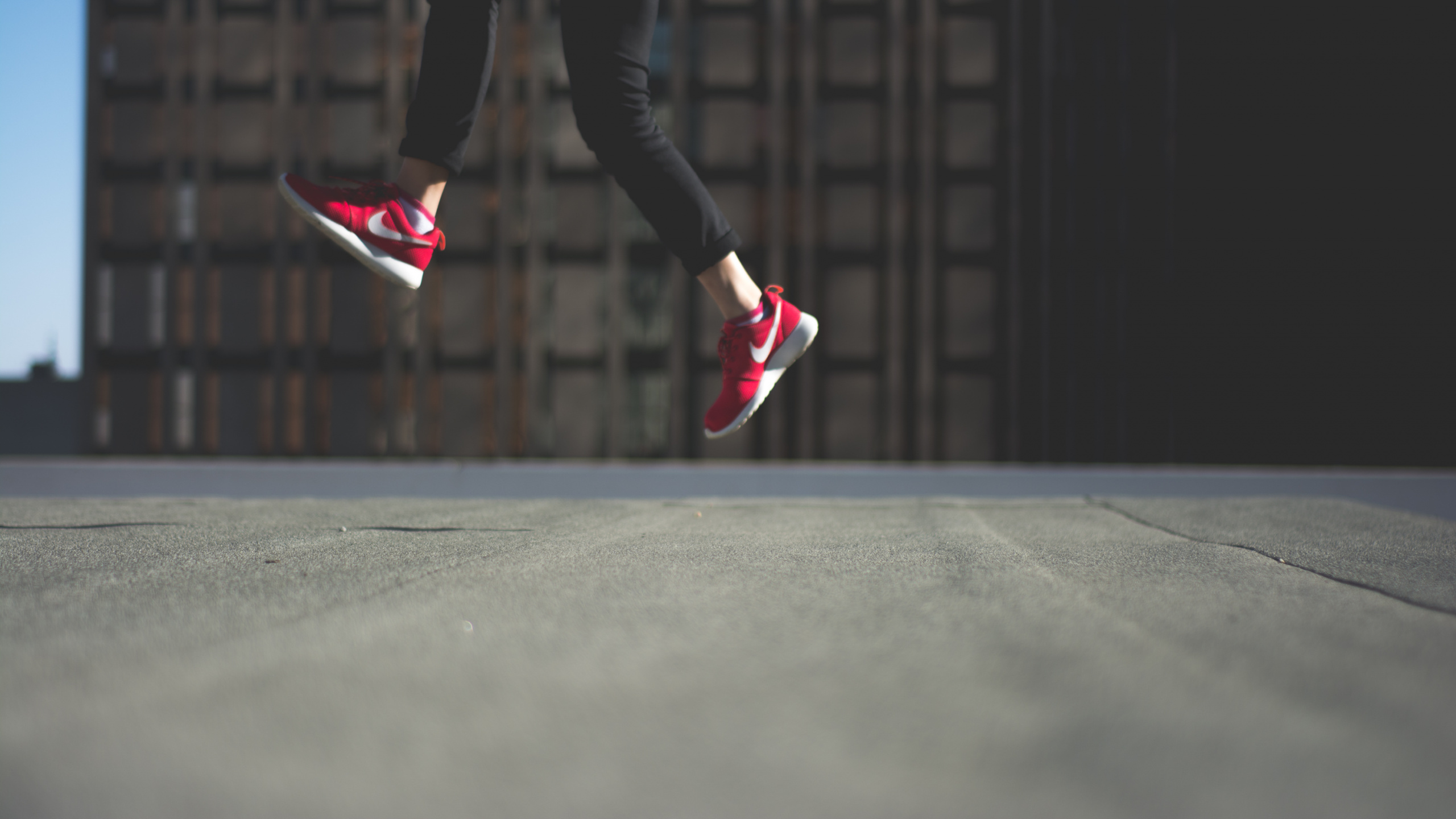 Personne en Pantalon Noir et Baskets Nike Roses Sautant Sur Une Route Goudronnée Noire. Wallpaper in 2560x1440 Resolution