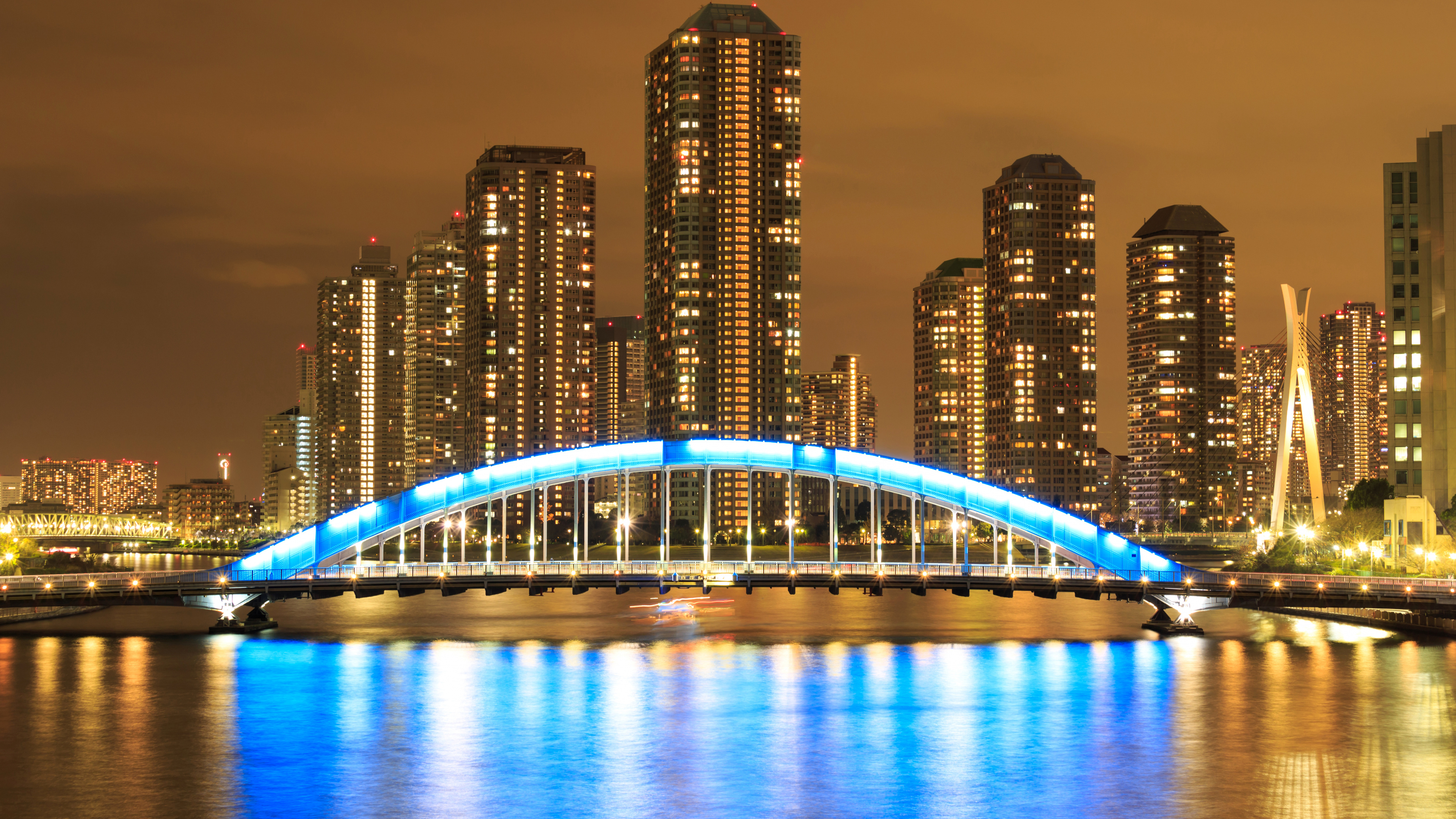 Beleuchtete Brücke Über Gewässer in Der Nähe Von Stadtgebäuden Während Der Nacht. Wallpaper in 3840x2160 Resolution