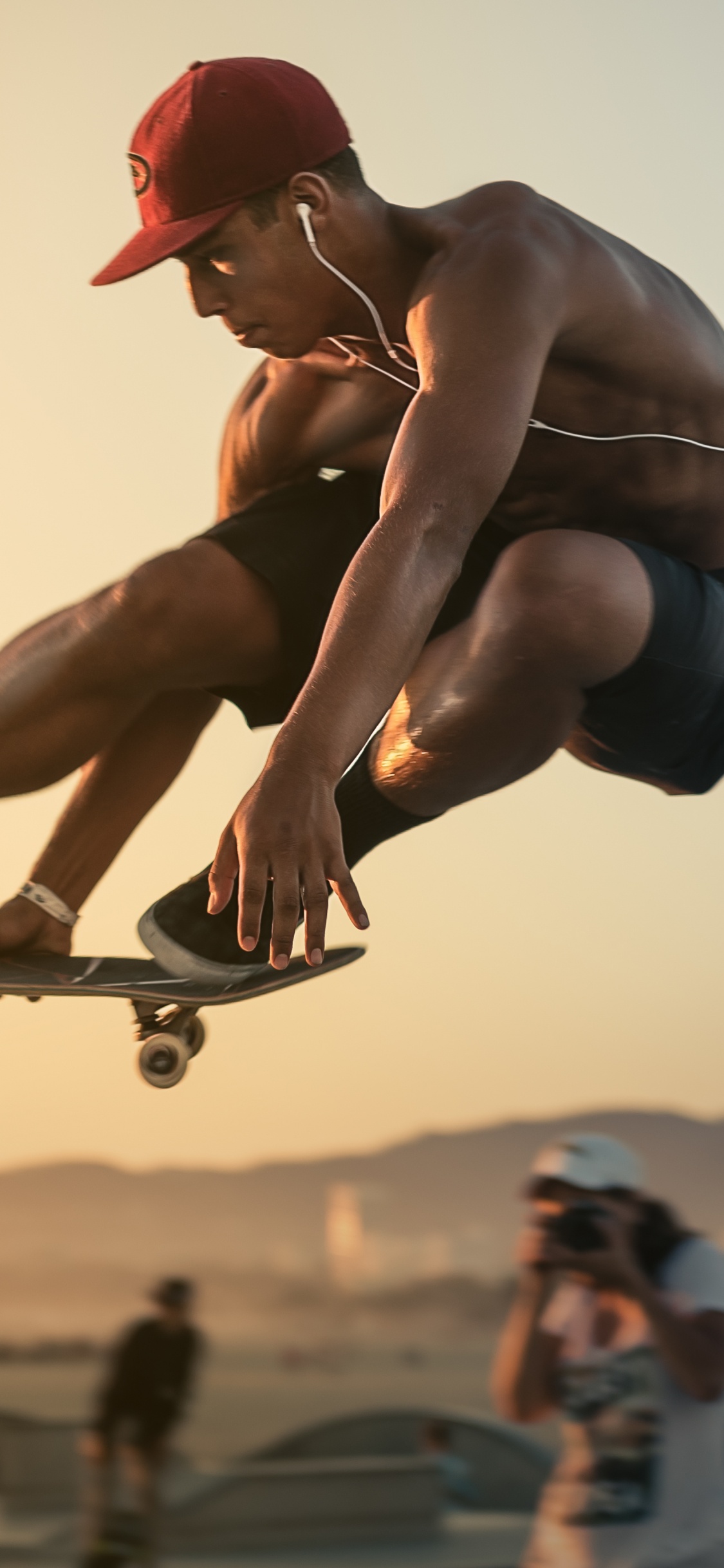 Man in Red Cap and Blue Shorts Doing Stunts. Wallpaper in 1125x2436 Resolution