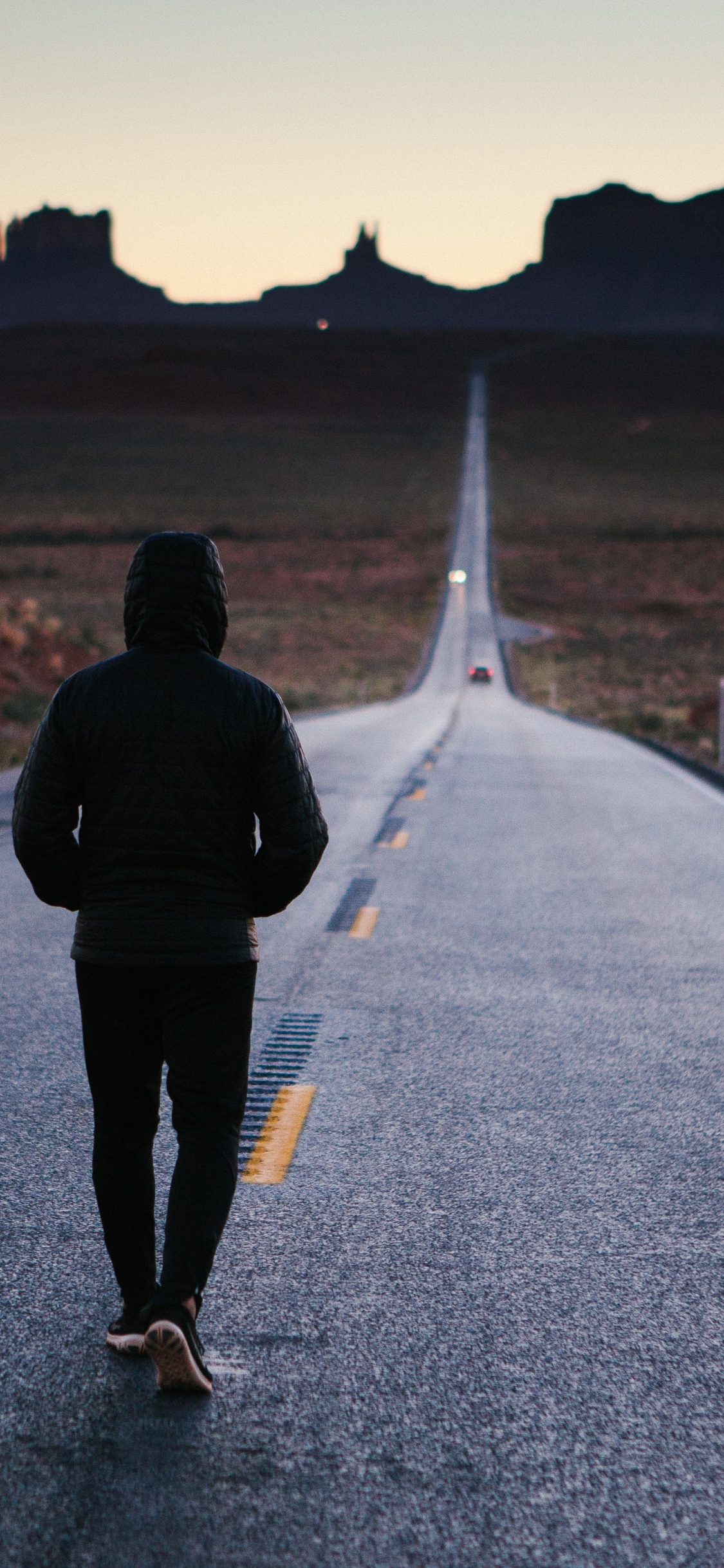 Hombre de Chaqueta Negra Caminando Por la Carretera Durante el Día. Wallpaper in 1125x2436 Resolution