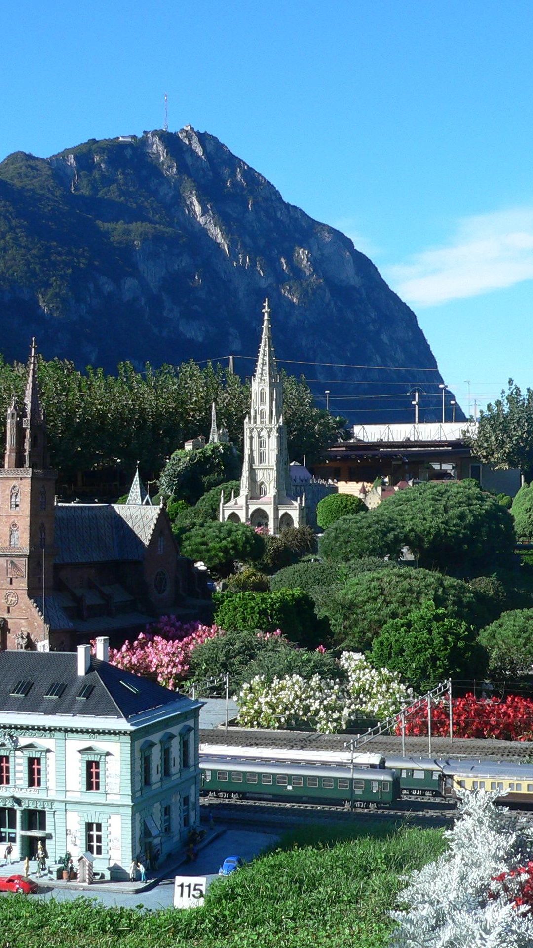 Weißes Und Braunes Betongebäude in Der Nähe Von Grünen Bäumen Und Bergen Unter Blauem Himmel Tagsüber. Wallpaper in 1080x1920 Resolution