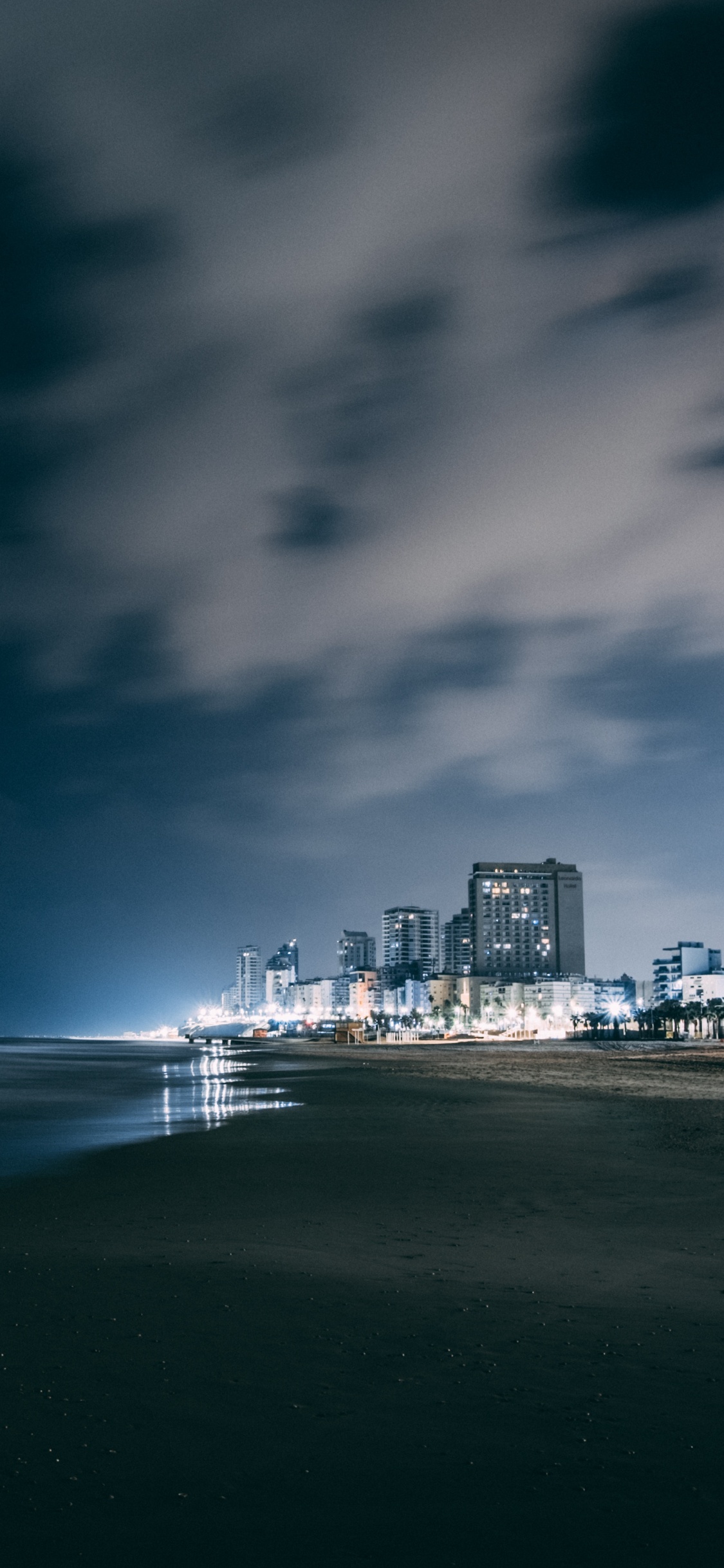 Horizonte de la Ciudad a Través Del Cuerpo de Agua Durante la Noche.. Wallpaper in 1125x2436 Resolution