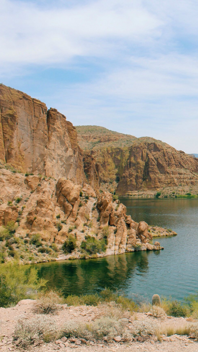 Brown Rocky Mountain Beside Blue Sea Under Blue Sky During Daytime. Wallpaper in 750x1334 Resolution