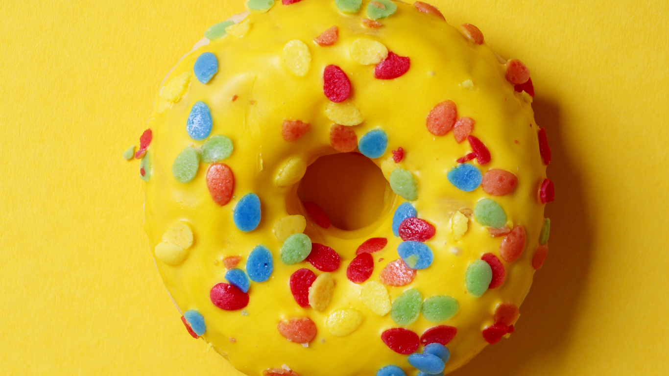 Donut Con Chispitas Sobre Superficie Amarilla. Wallpaper in 1366x768 Resolution