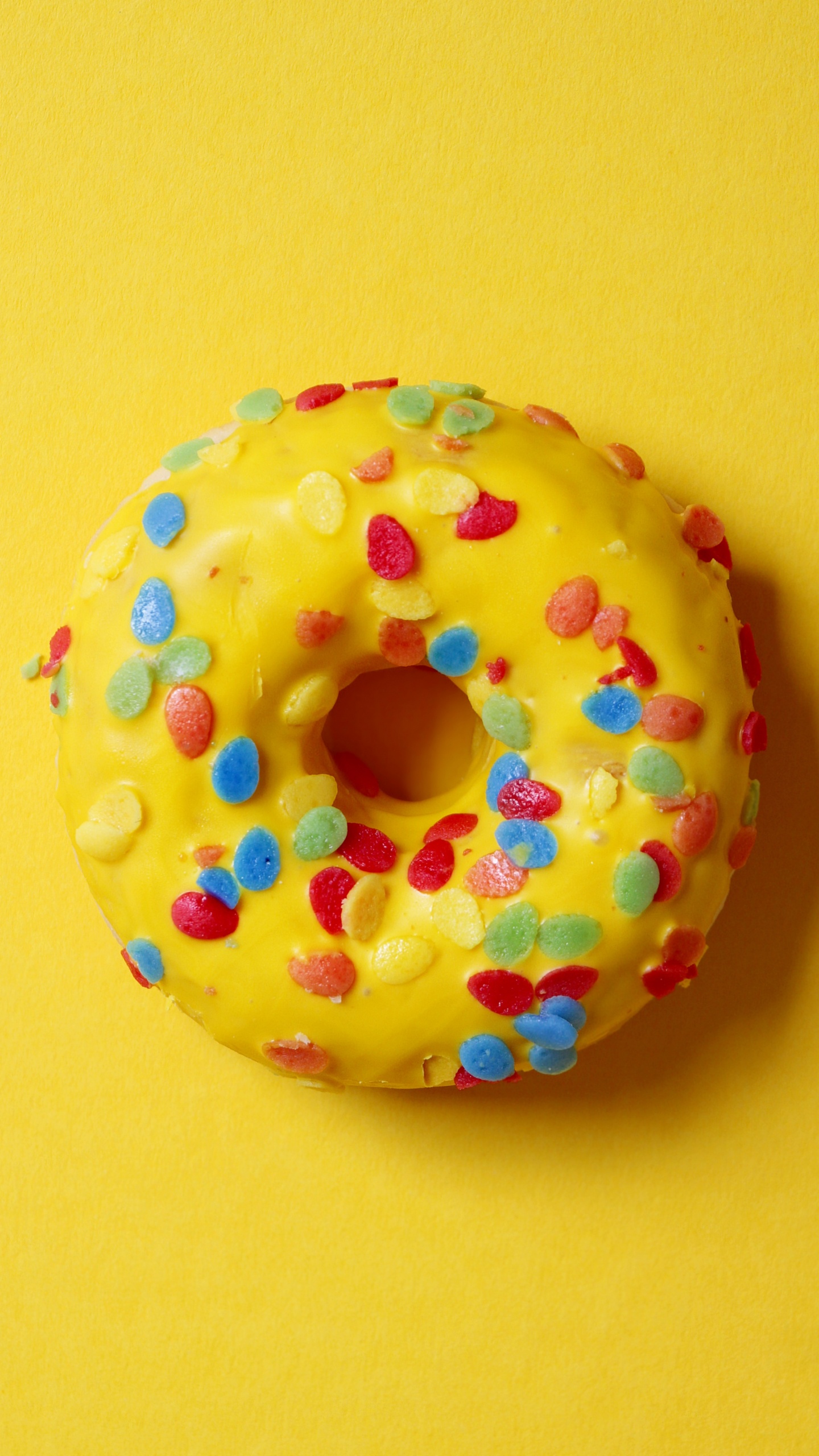 Doughnut With Sprinkles on Yellow Surface. Wallpaper in 1440x2560 Resolution