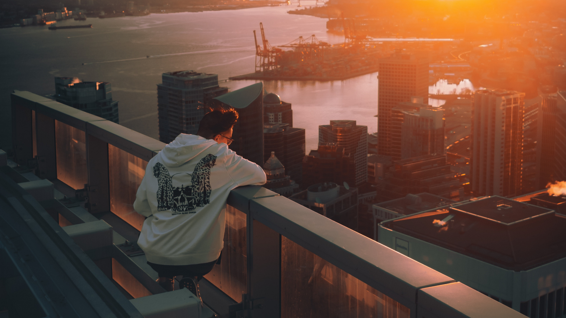 Man in White Hoodie Sitting on Brown Wooden Fence Looking at City Skyline During Sunset. Wallpaper in 1920x1080 Resolution