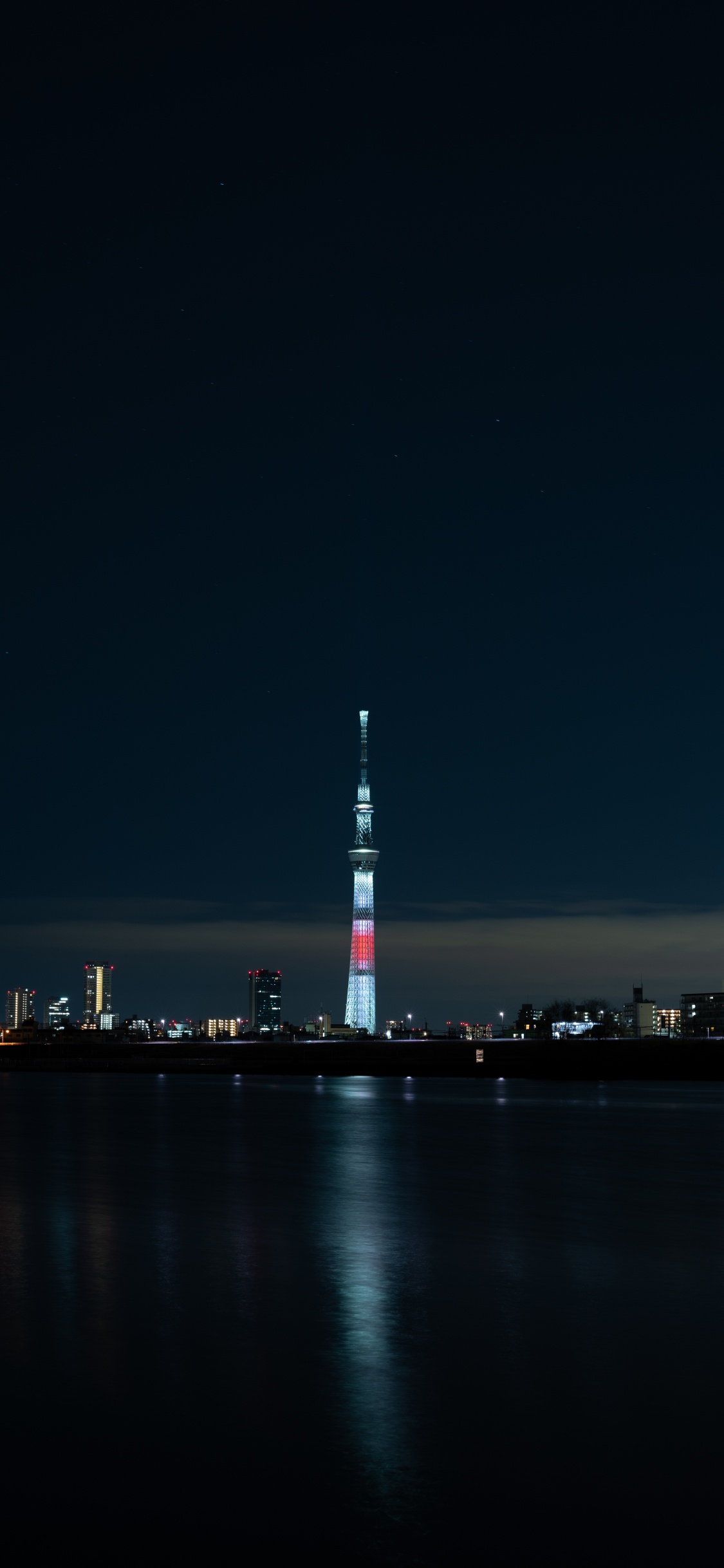 White and Red Tower Near Body of Water During Night Time. Wallpaper in 1125x2436 Resolution