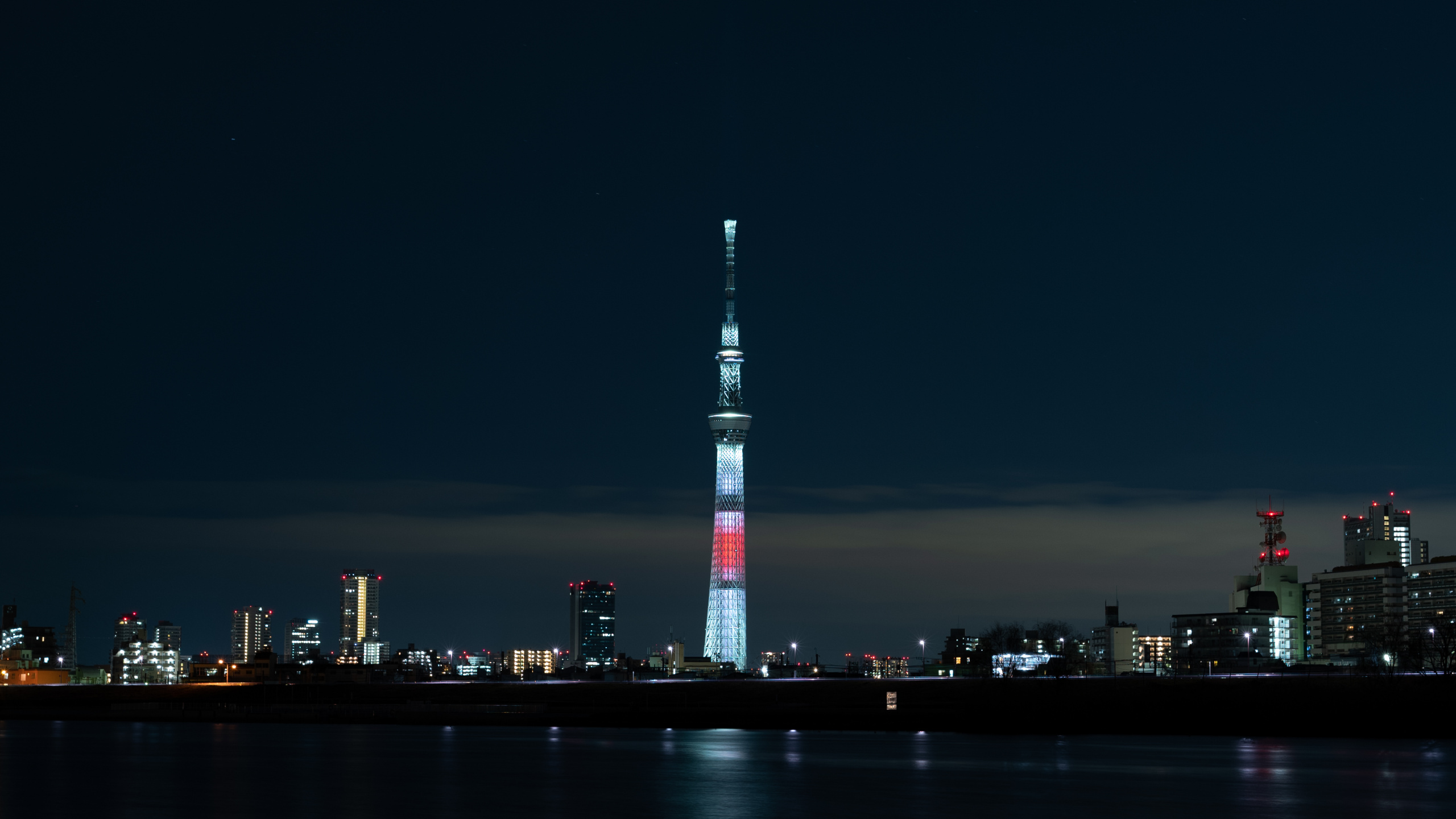 White and Red Tower Near Body of Water During Night Time. Wallpaper in 2560x1440 Resolution