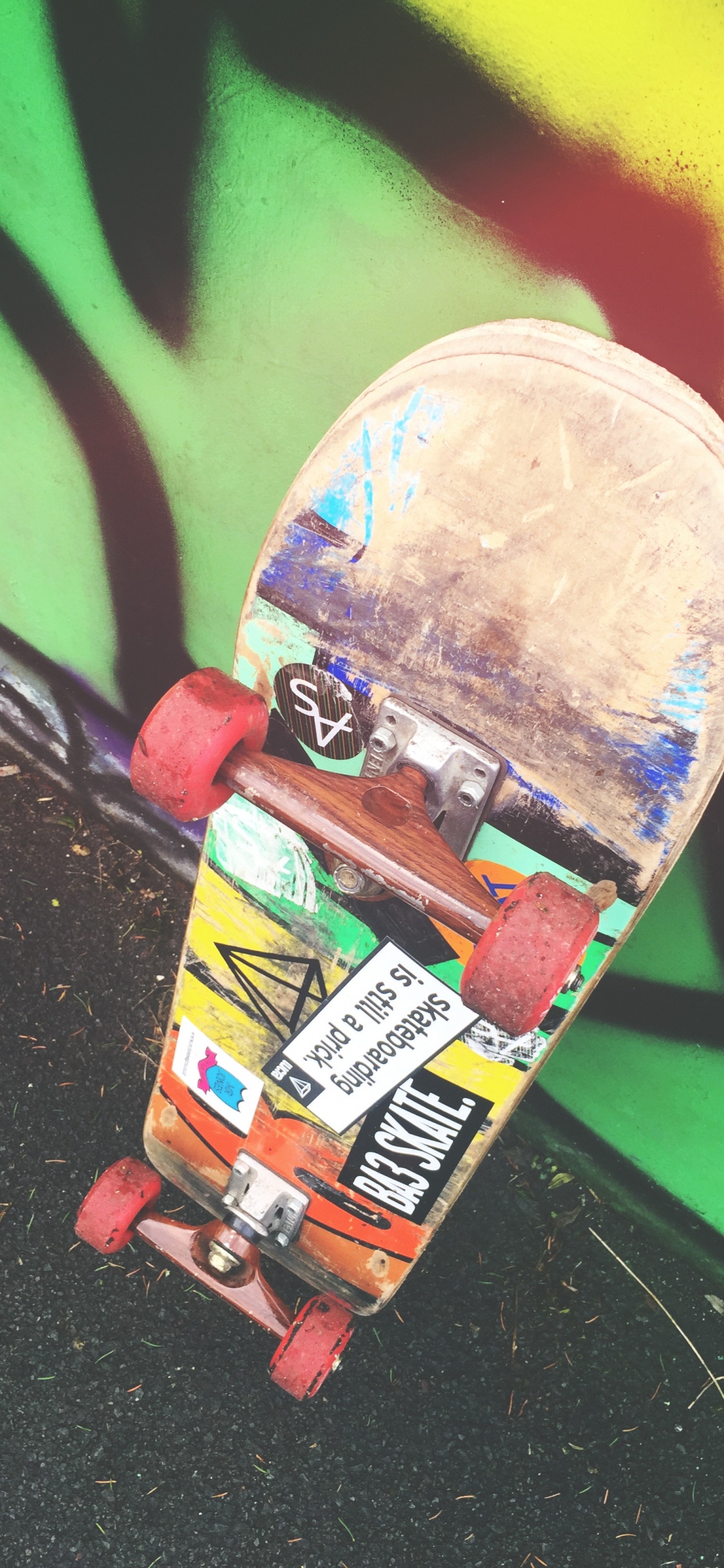 Skateboard Rouge et Jaune Sur Mur Vert. Wallpaper in 1125x2436 Resolution