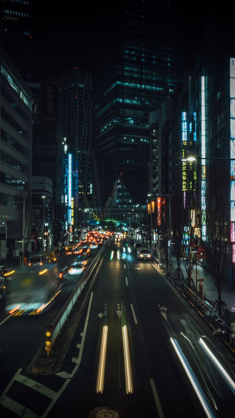 Autos Auf Der Straße Zwischen Hochhäusern Während Der Nacht. Wallpaper in 750x1334 Resolution