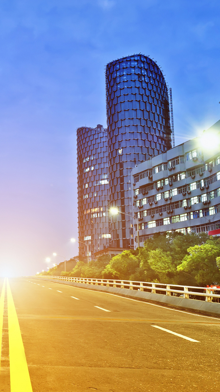 Gray Concrete Road Between Green Trees and High Rise Buildings During Daytime. Wallpaper in 750x1334 Resolution