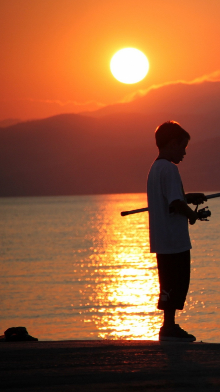 Homme en Chemise Blanche et Short Noir Pêchant en Mer Pendant le Coucher du Soleil. Wallpaper in 750x1334 Resolution