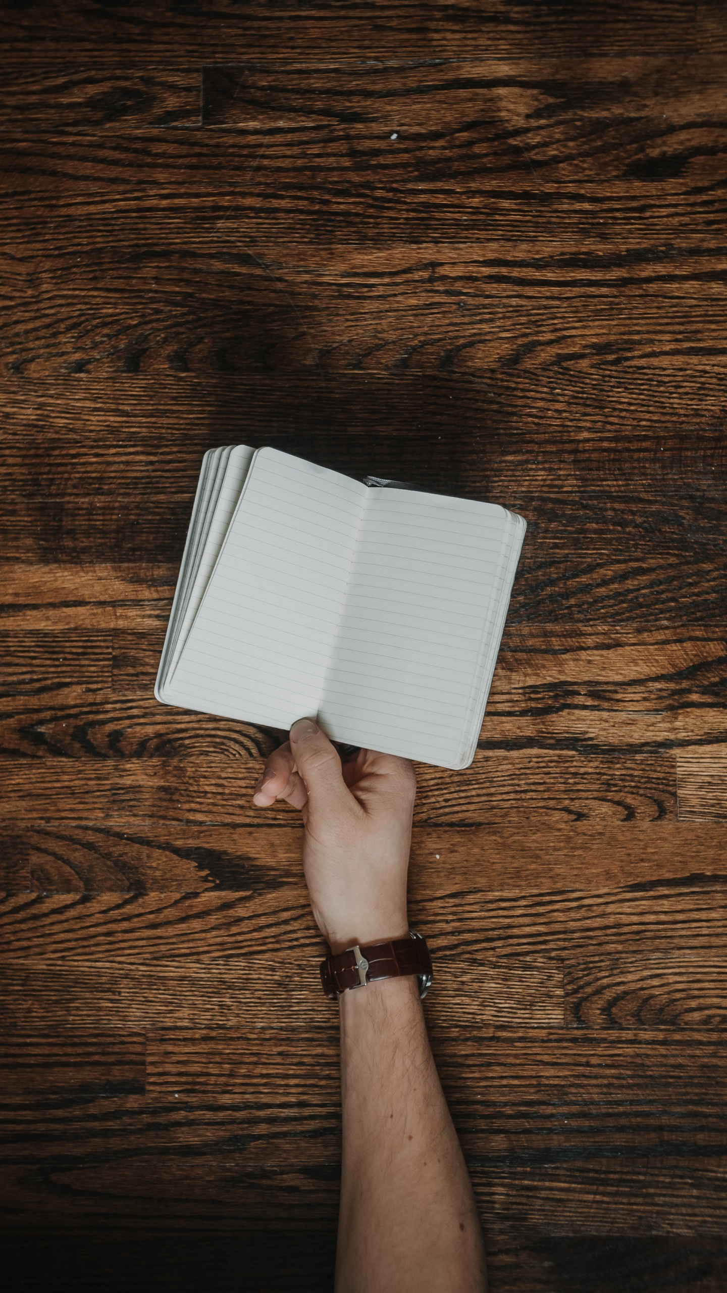Person Holding White Paper on Brown Wooden Floor. Wallpaper in 1440x2560 Resolution