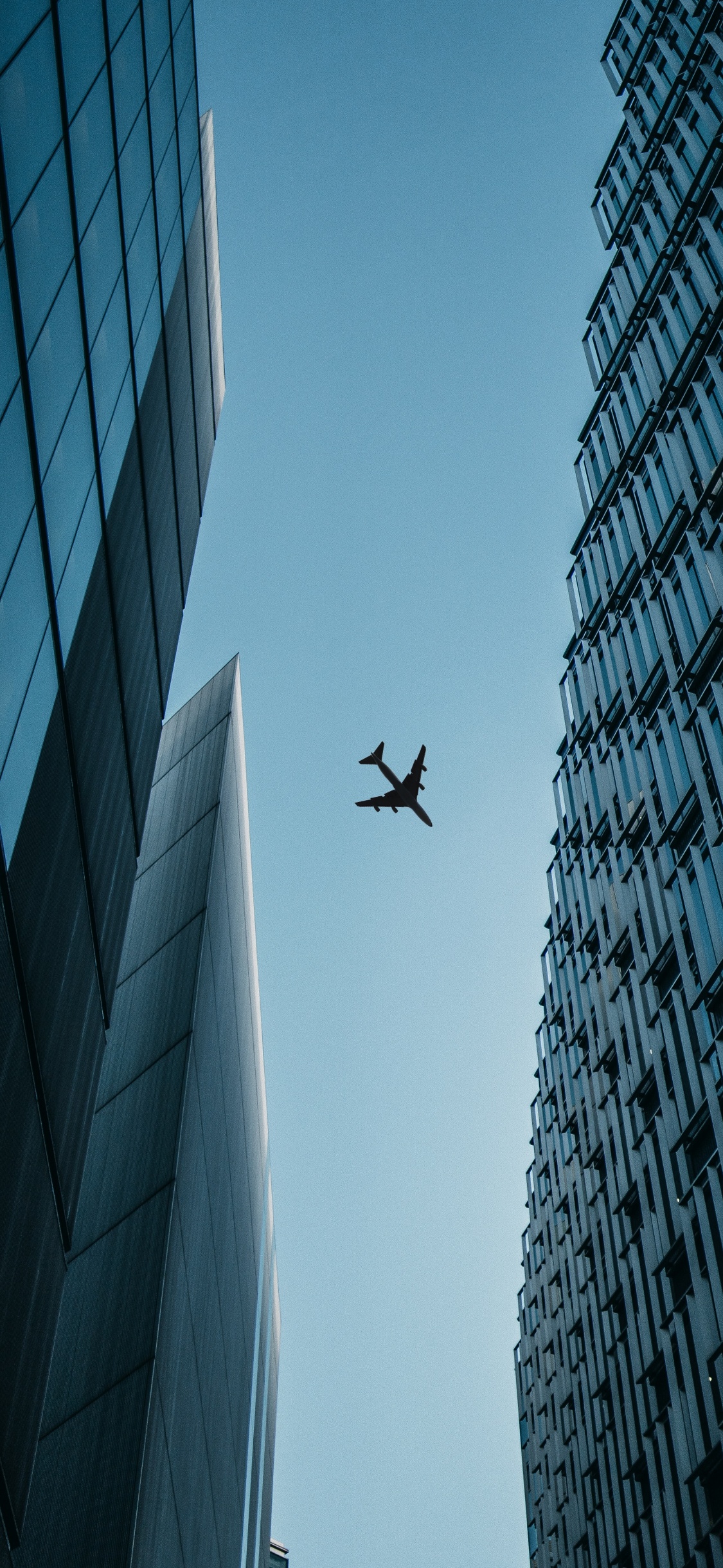 Airplane Flying Over The Building During Daytime. Wallpaper in 1125x2436 Resolution