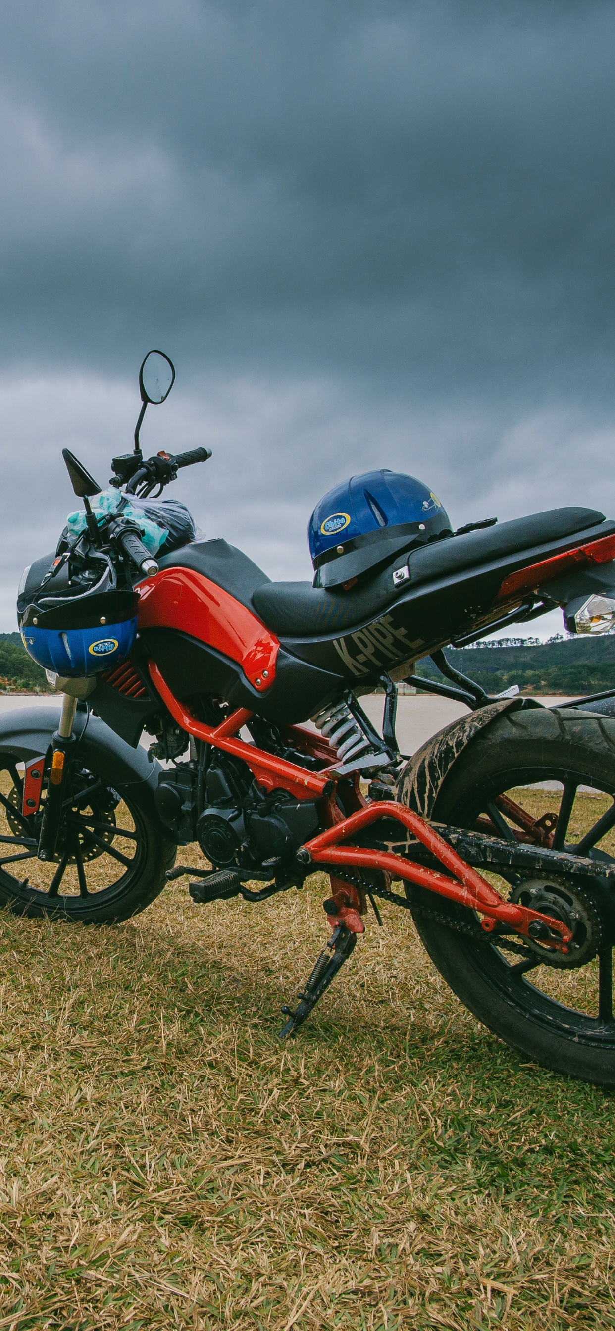 Moto Standard Rouge et Noir Sur Champ Brun Sous Ciel Nuageux Gris. Wallpaper in 1242x2688 Resolution