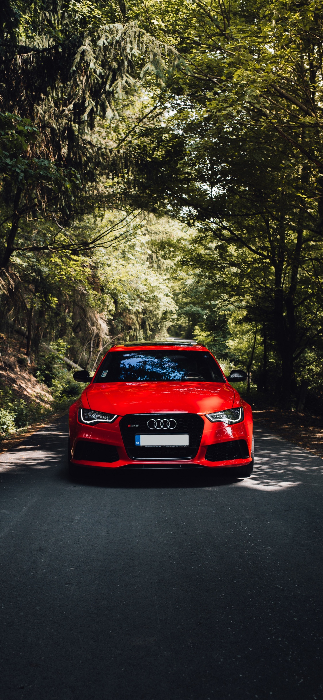 Rotes Auto Auf Der Straße Zwischen Bäumen Tagsüber. Wallpaper in 1125x2436 Resolution