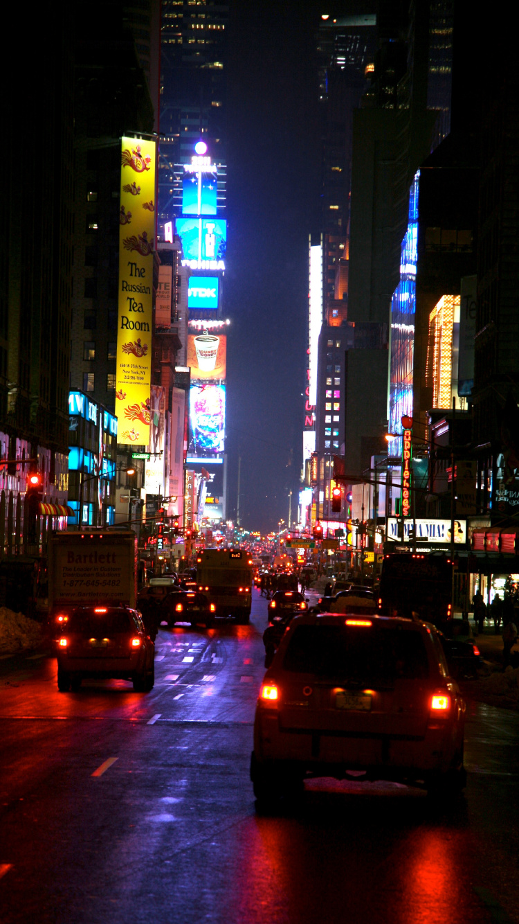 Autos Auf Der Straße Zwischen Hochhäusern Während Der Nacht. Wallpaper in 750x1334 Resolution