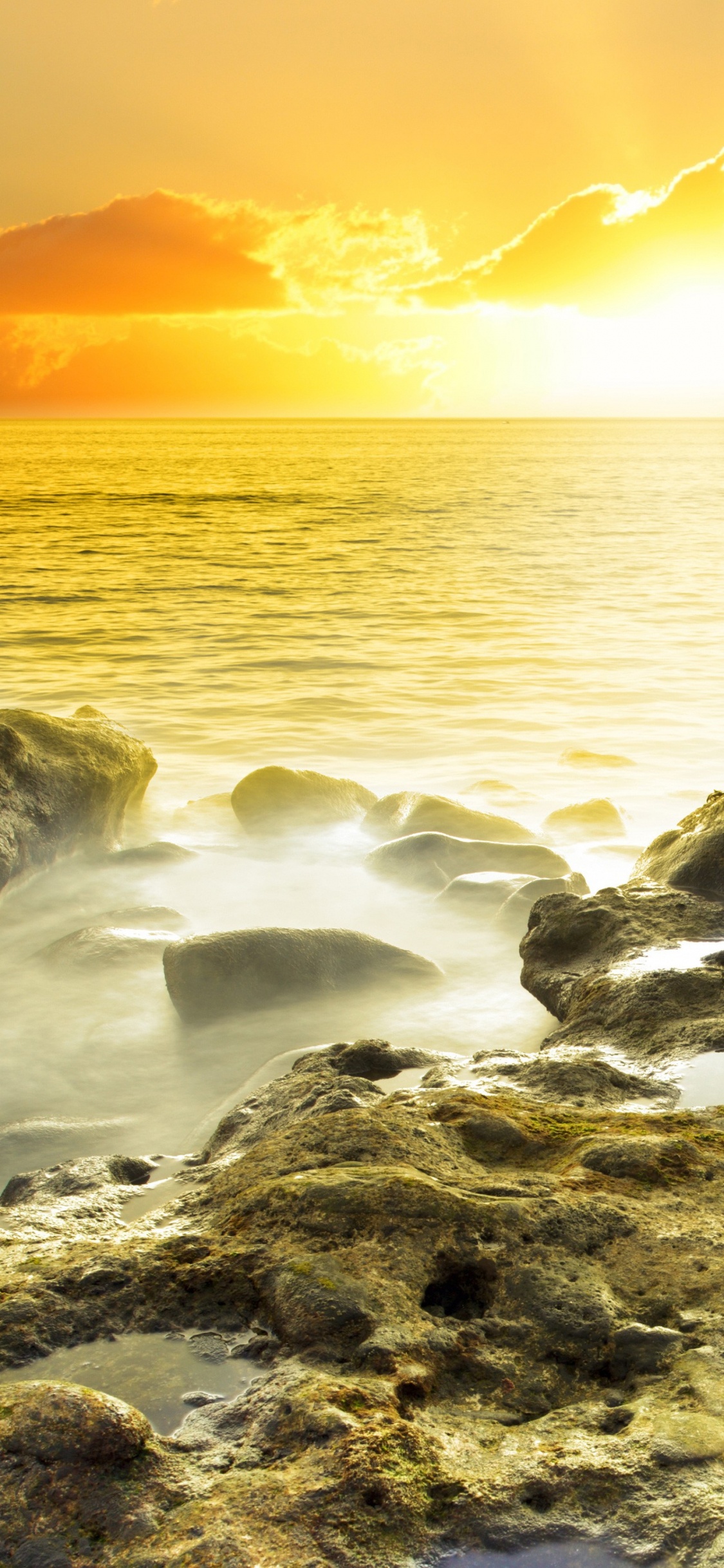Graue Felsen Auf Gewässer Während Des Sonnenuntergangs. Wallpaper in 1125x2436 Resolution