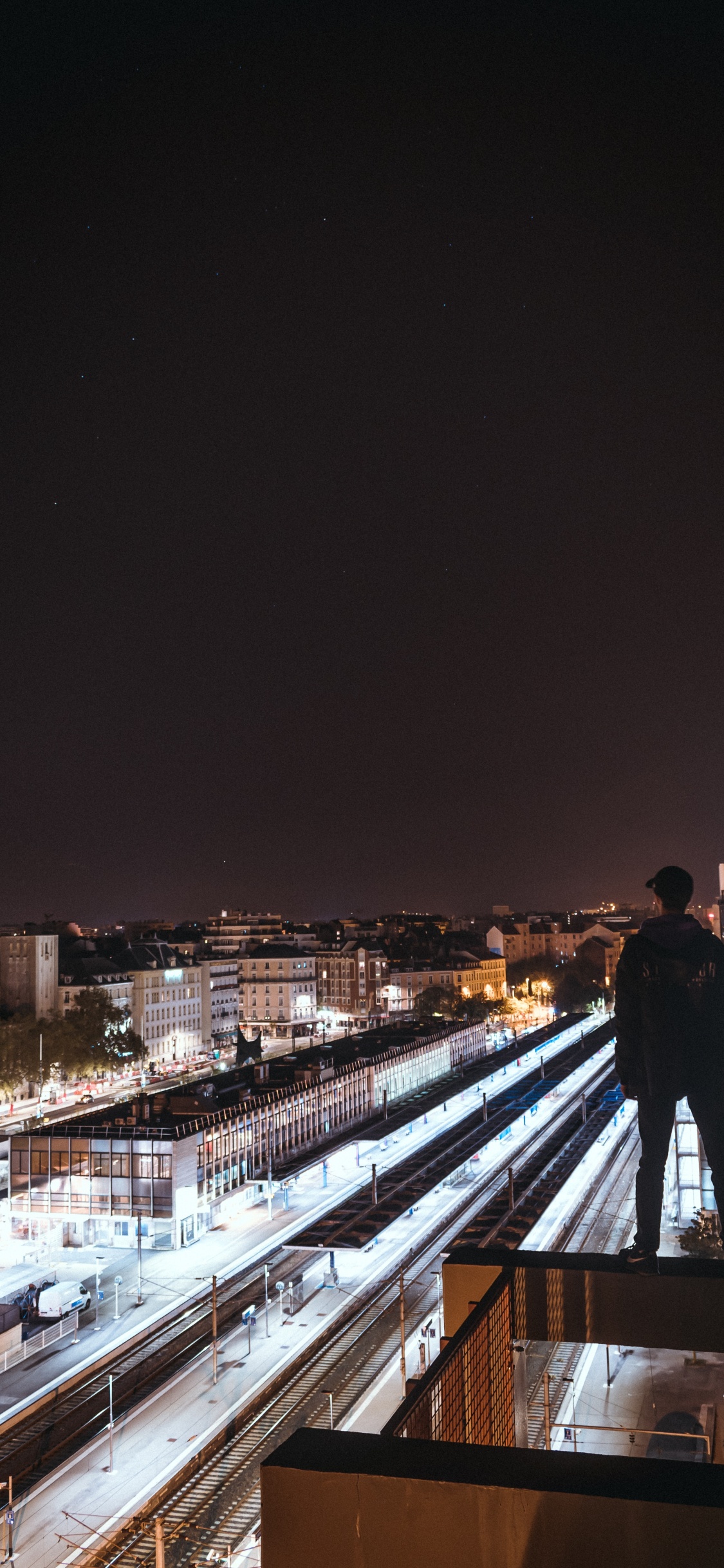Man in Black Jacket Standing on Brown Wooden Bridge During Night Time. Wallpaper in 1125x2436 Resolution