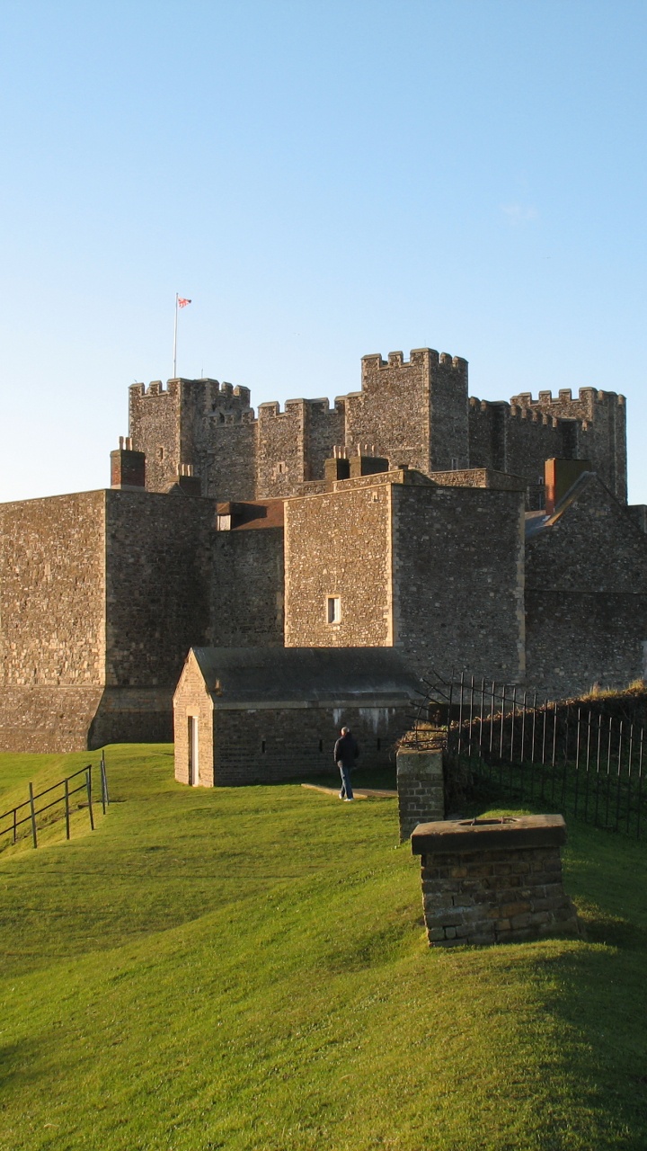 Graues Betongebäude Auf Grüner Wiese Unter Blauem Himmel Tagsüber. Wallpaper in 720x1280 Resolution
