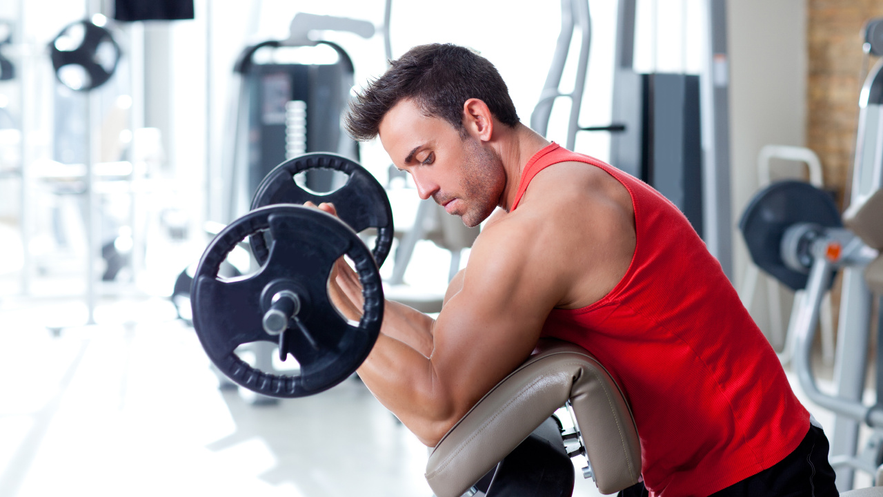 Man in Red Tank Top Sitting on Black and Gray Exercise Equipment. Wallpaper in 1280x720 Resolution