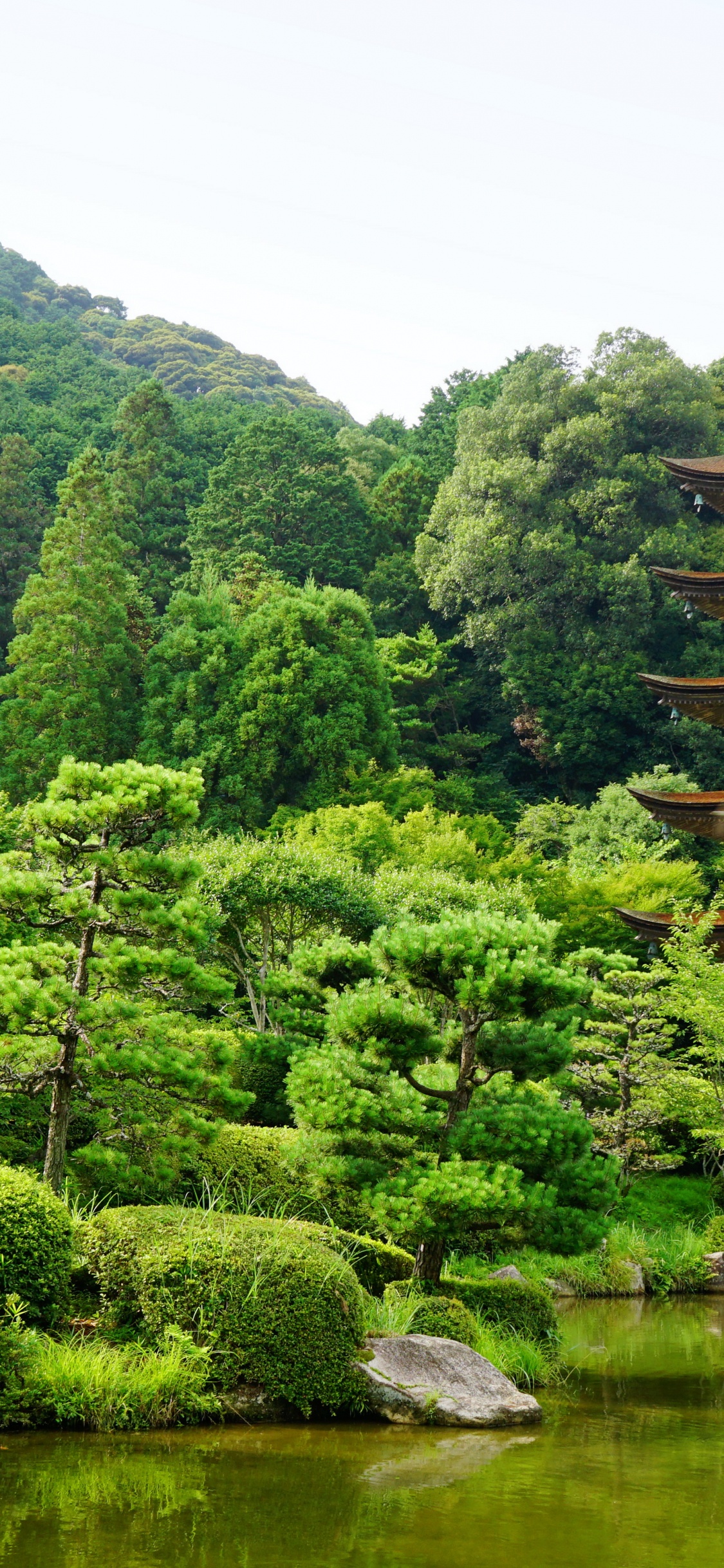 Brown Temple Near Green Trees and Lake During Daytime. Wallpaper in 1125x2436 Resolution