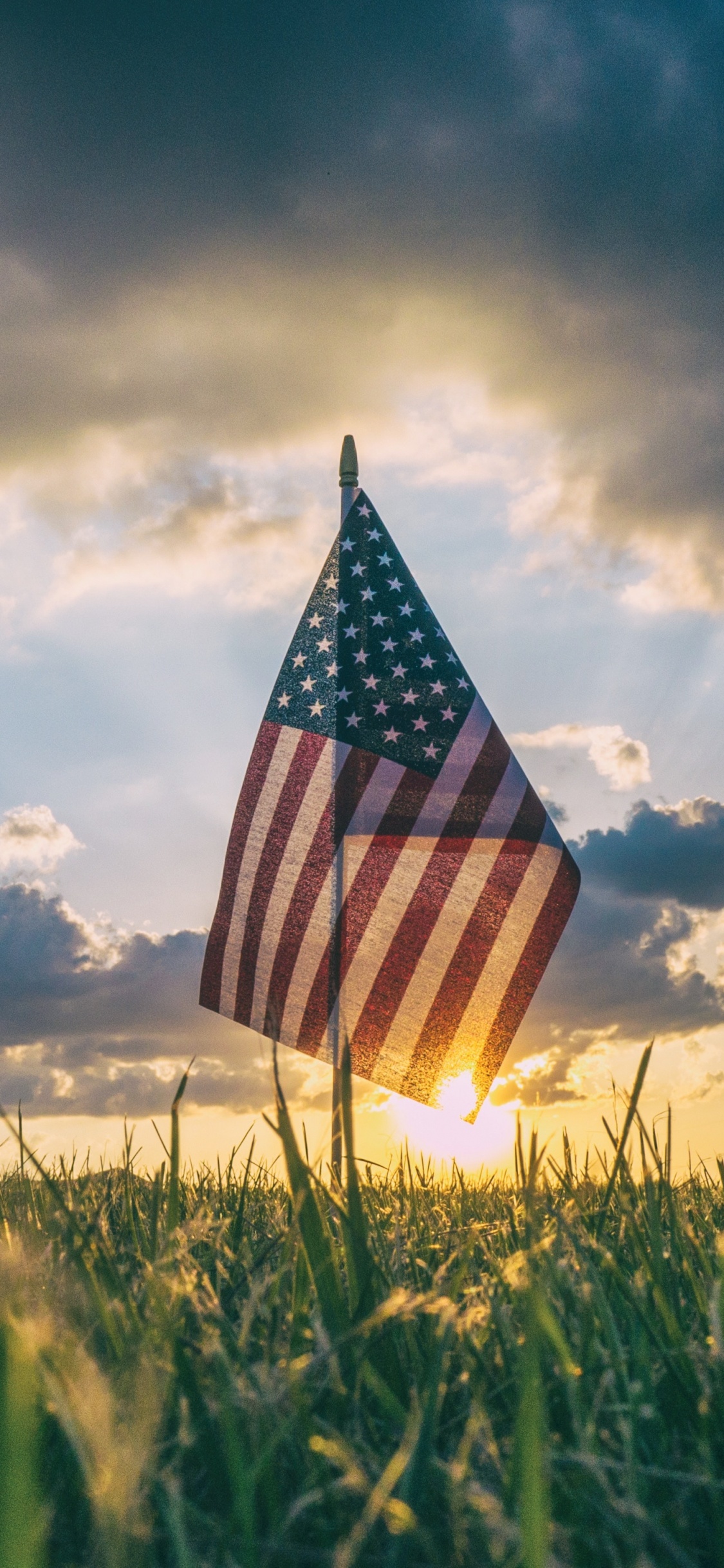 Nous un Drapeau Sur le Terrain D'herbe Verte Sous un Ciel Nuageux Pendant la Journée. Wallpaper in 1125x2436 Resolution