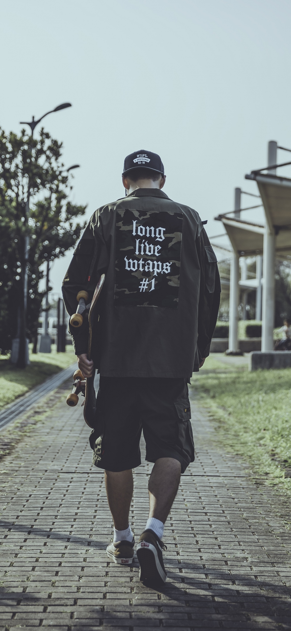 Hombre Con Capucha Negra Caminando Sobre la Acera Durante el Día. Wallpaper in 1125x2436 Resolution