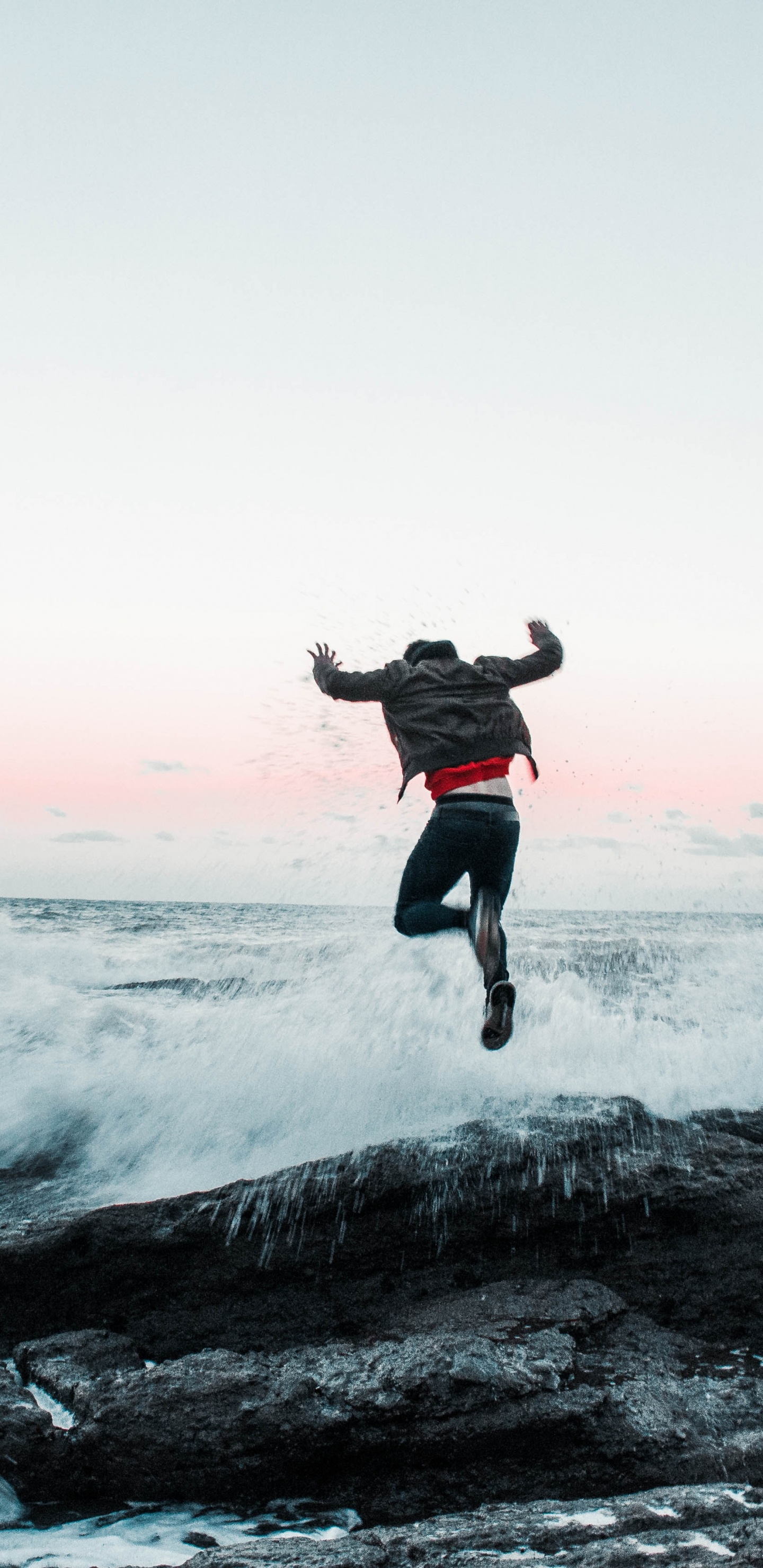 Man in Black Jacket and Pants Jumping on Rocky Shore During Daytime. Wallpaper in 1440x2960 Resolution