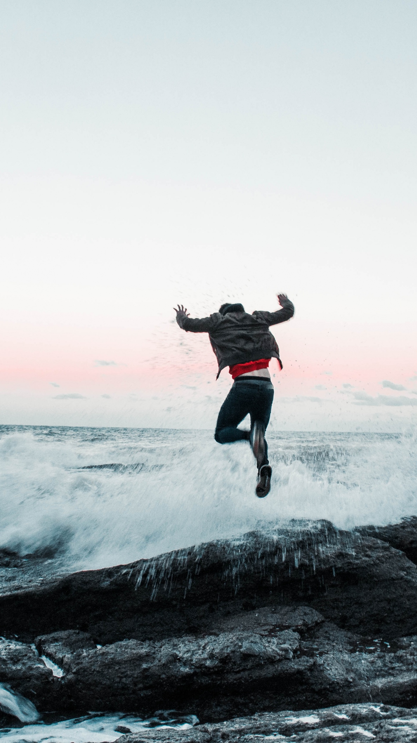 Mann in Schwarzer Jacke Und Hose, Der Tagsüber Auf Felsigem Ufer Springt. Wallpaper in 1440x2560 Resolution