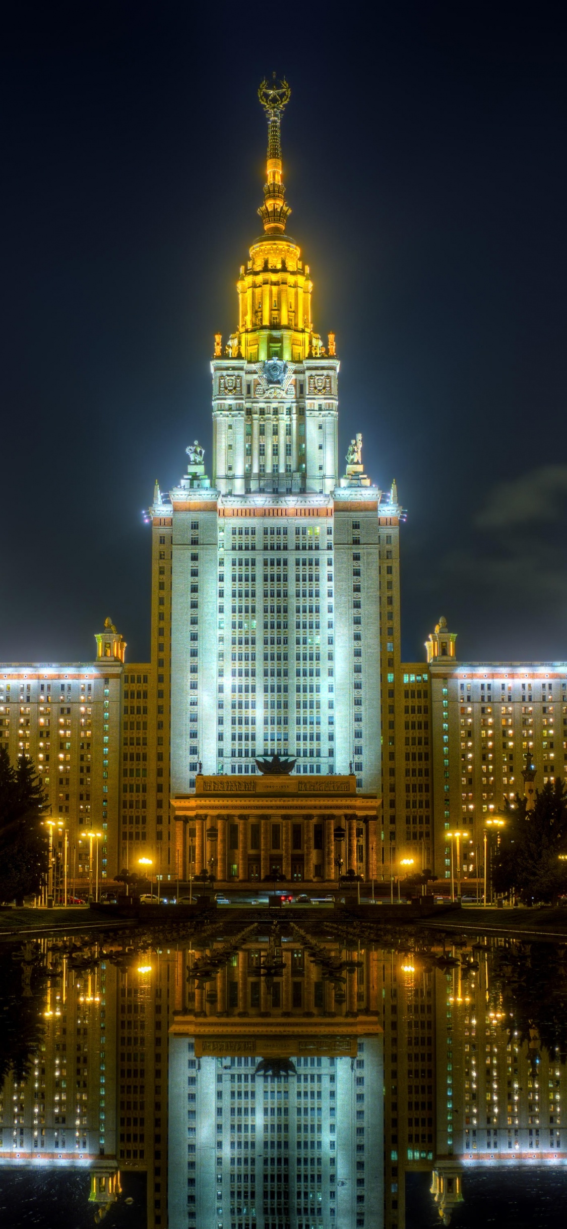 Edificio Iluminado Cerca Del Cuerpo de Agua Durante la Noche.. Wallpaper in 1125x2436 Resolution