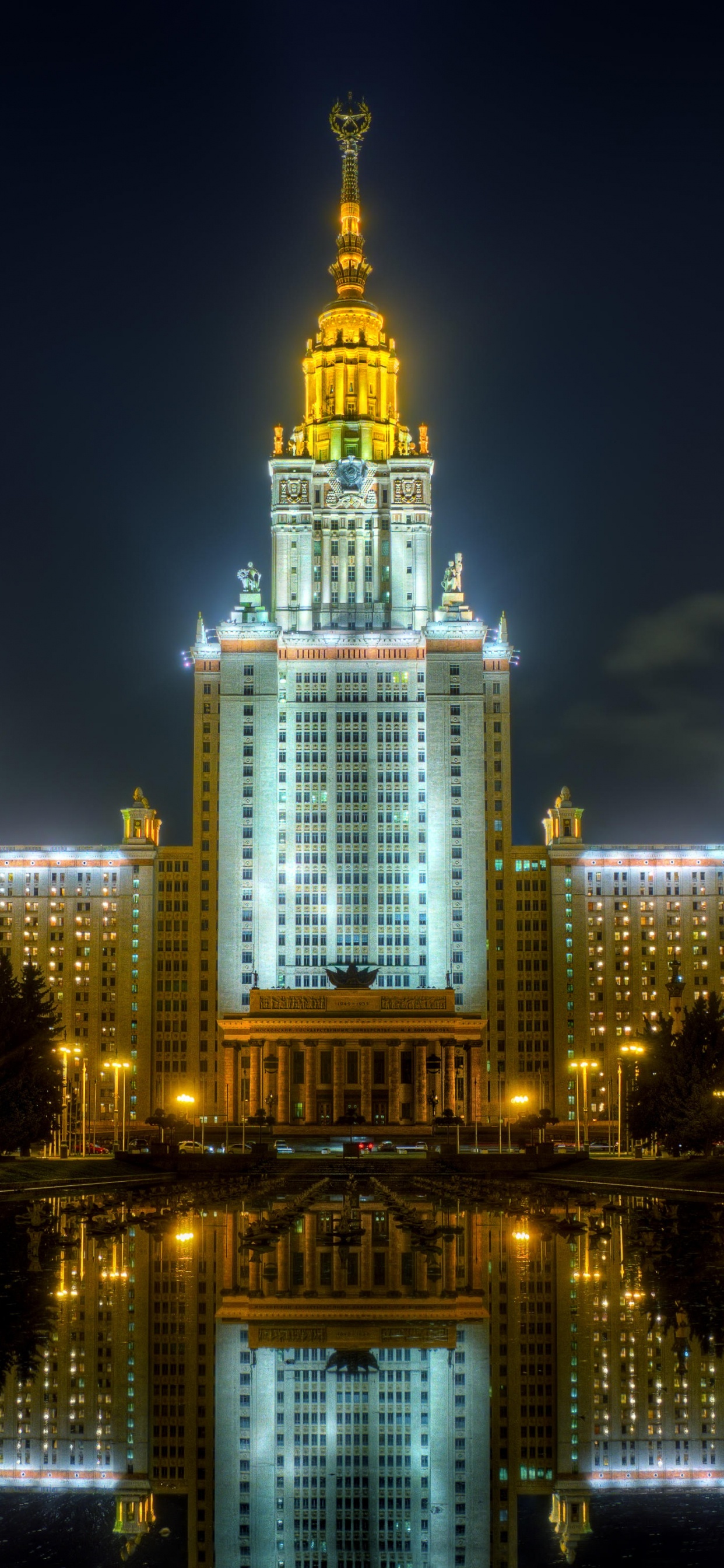 Edificio Iluminado Cerca Del Cuerpo de Agua Durante la Noche.. Wallpaper in 1242x2688 Resolution