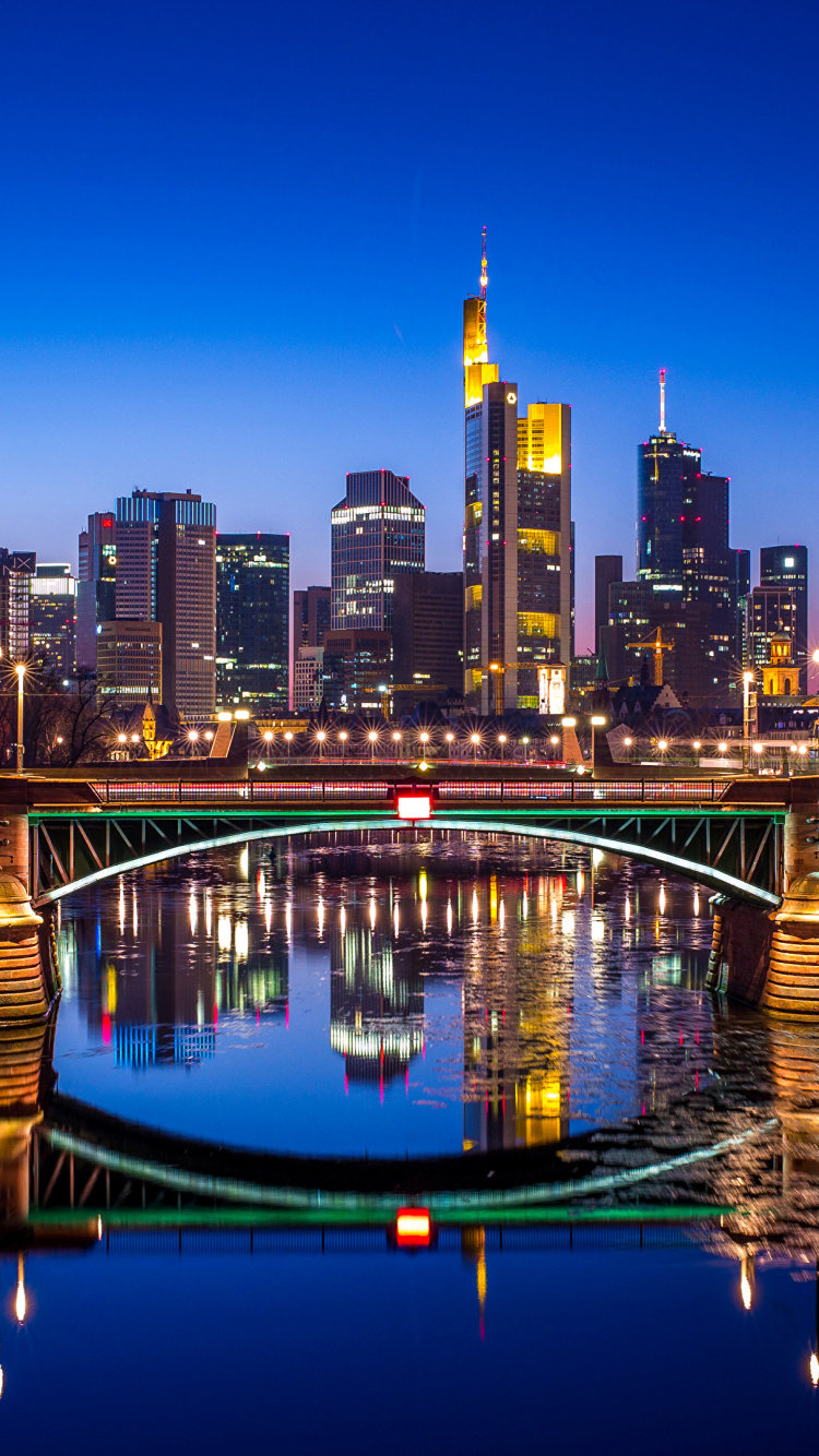 Pont Au-dessus de L'eau Près Des Bâtiments de la Ville Pendant la Nuit. Wallpaper in 750x1334 Resolution