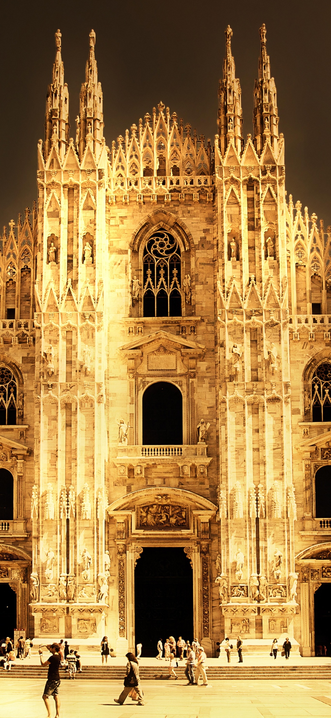 Leute, Die Nachts in Der Nähe Eines Braunen Betongebäudes Gehen. Wallpaper in 1125x2436 Resolution