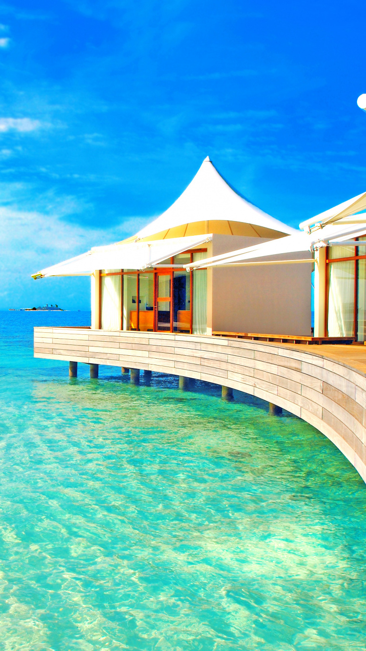 Maison de Plage en Bois Marron Sur Mer Bleue Sous Ciel Bleu Pendant la Journée. Wallpaper in 750x1334 Resolution