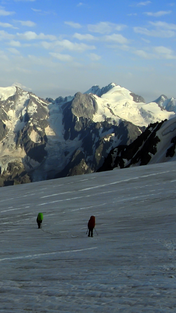 Persona en Chaqueta Verde Caminando Sobre el Campo Cubierto de Nieve Durante el Día. Wallpaper in 750x1334 Resolution