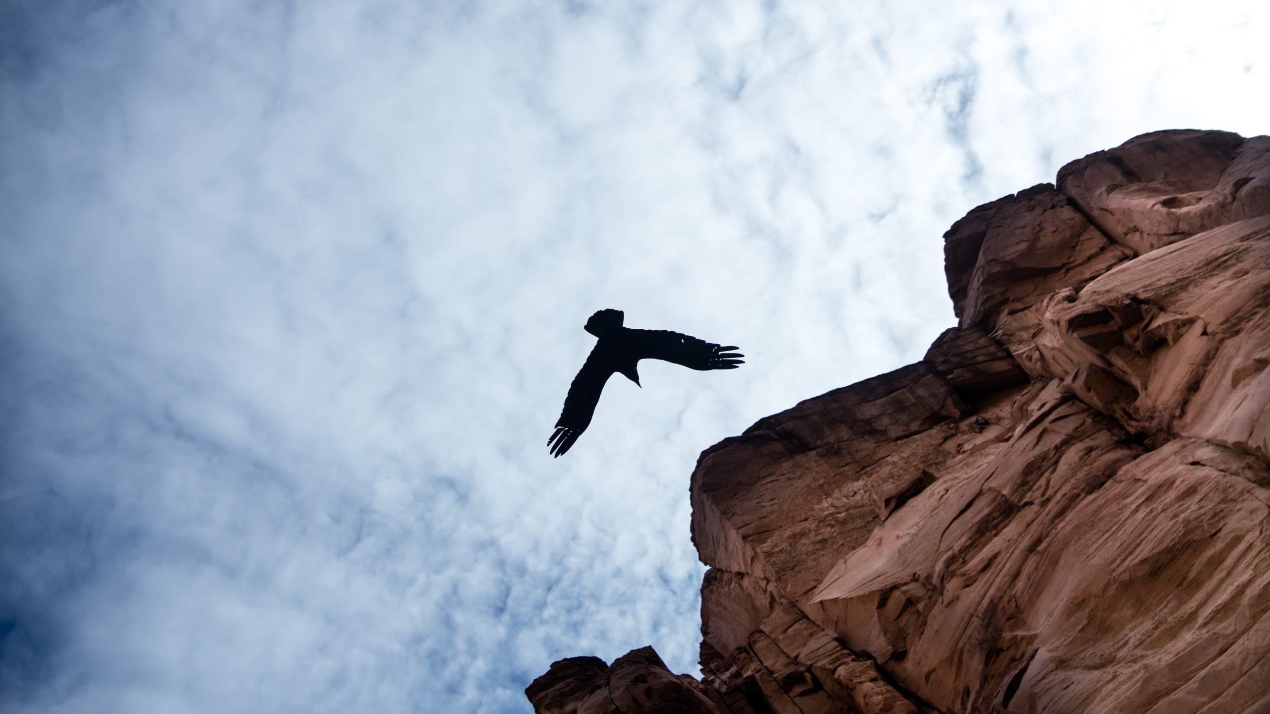 Man Jumping on Brown Rock Formation Under White Clouds and Blue Sky During Daytime. Wallpaper in 2560x1440 Resolution