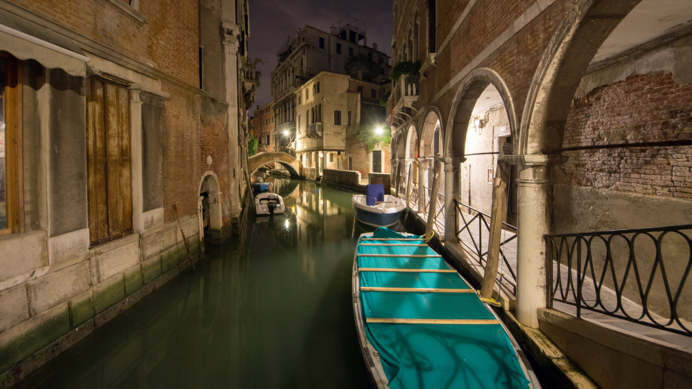 Bateau Bleu Sur la Rivière Entre Bâtiment en Béton Brun Pendant la Journée. Wallpaper in 1366x768 Resolution