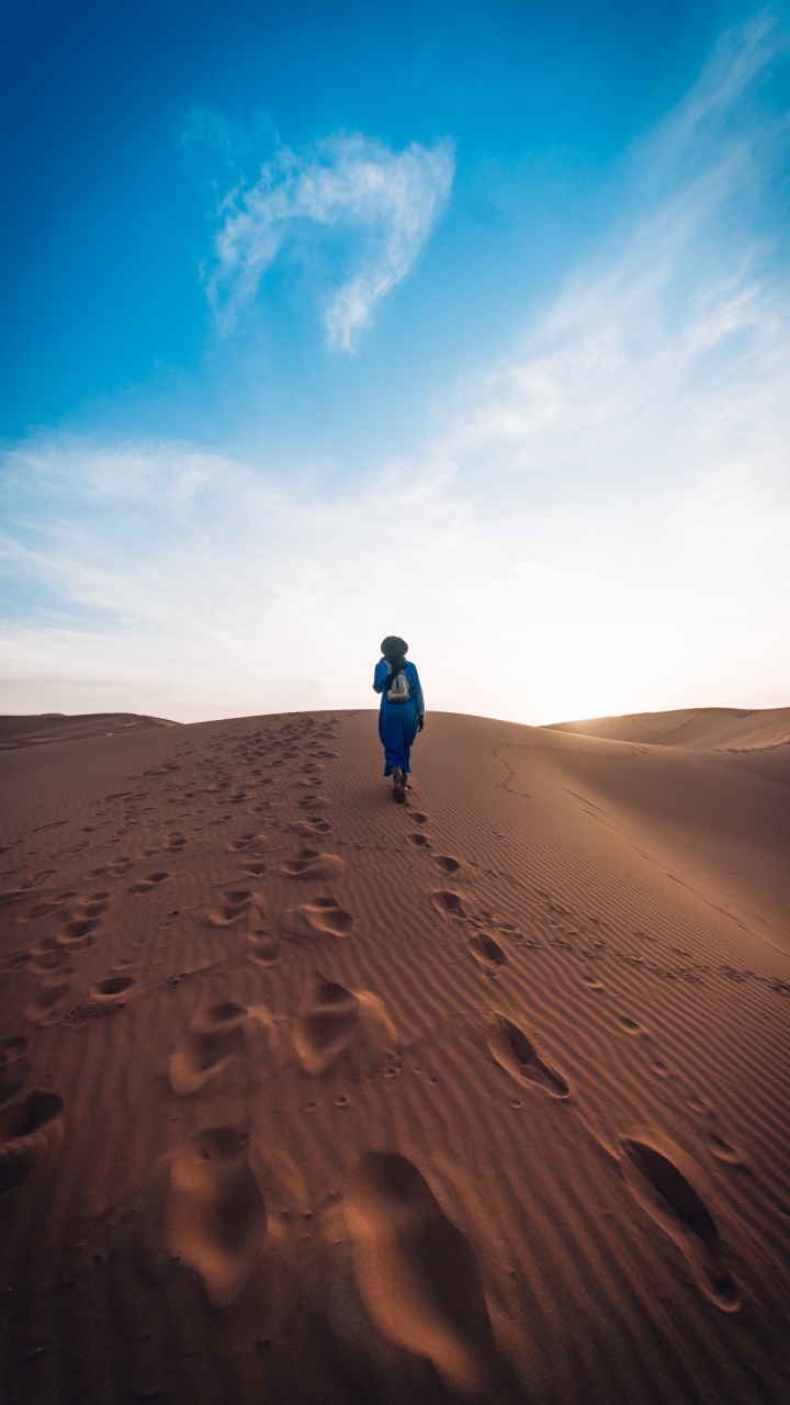 Person in Blauer Jacke, Die Tagsüber Auf Braunem Sand Unter Blauem Himmel Geht. Wallpaper in 720x1280 Resolution