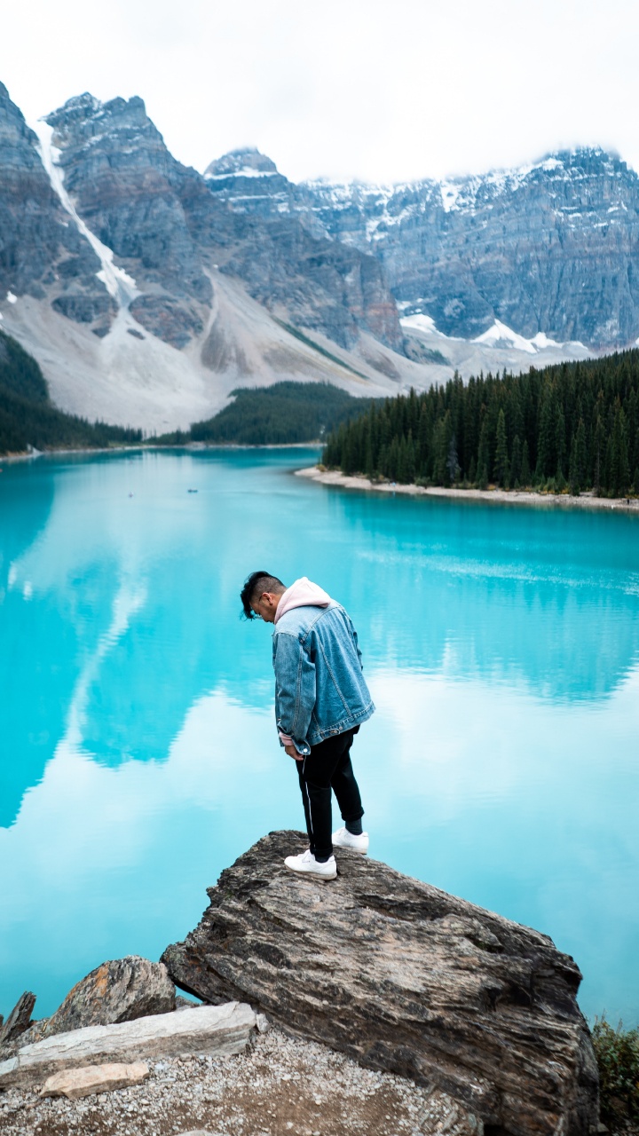 Homme en Chemise Blanche Debout Sur un Rocher Près du Lac Pendant la Journée. Wallpaper in 720x1280 Resolution