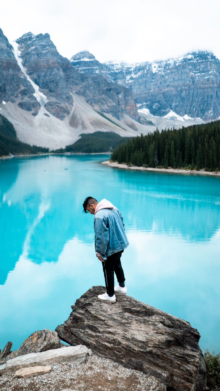 Homme en Chemise Blanche Debout Sur un Rocher Près du Lac Pendant la Journée. Wallpaper in 750x1334 Resolution