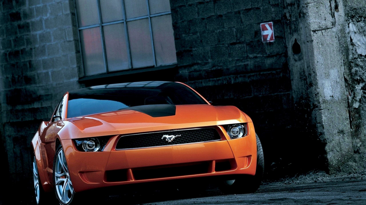 Orange Chevrolet Camaro Parked Beside Gray Brick Wall. Wallpaper in 1280x720 Resolution