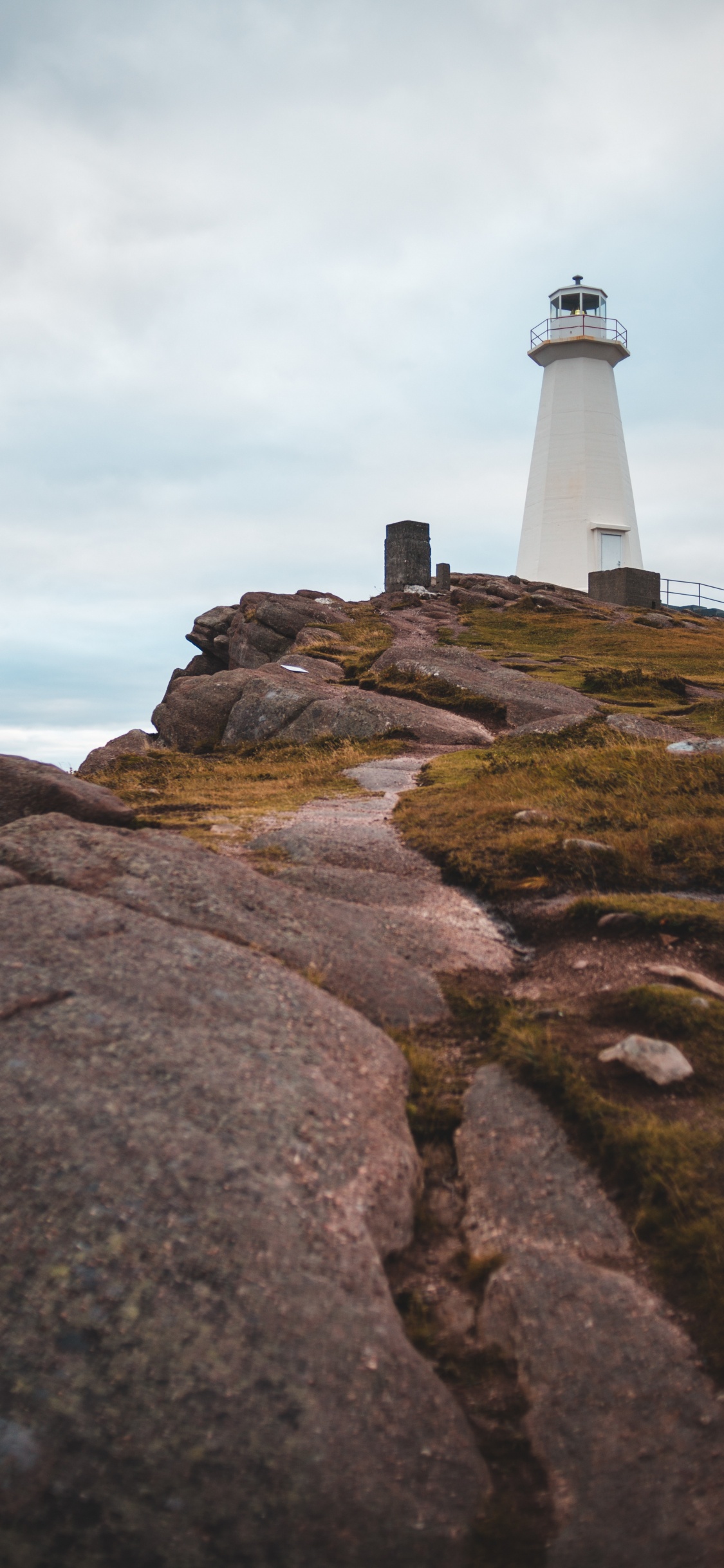 Weißer Und Schwarzer Leuchtturm Auf Braunem Felsigem Hügel Unter Weißem Bewölktem Himmel Tagsüber. Wallpaper in 1125x2436 Resolution