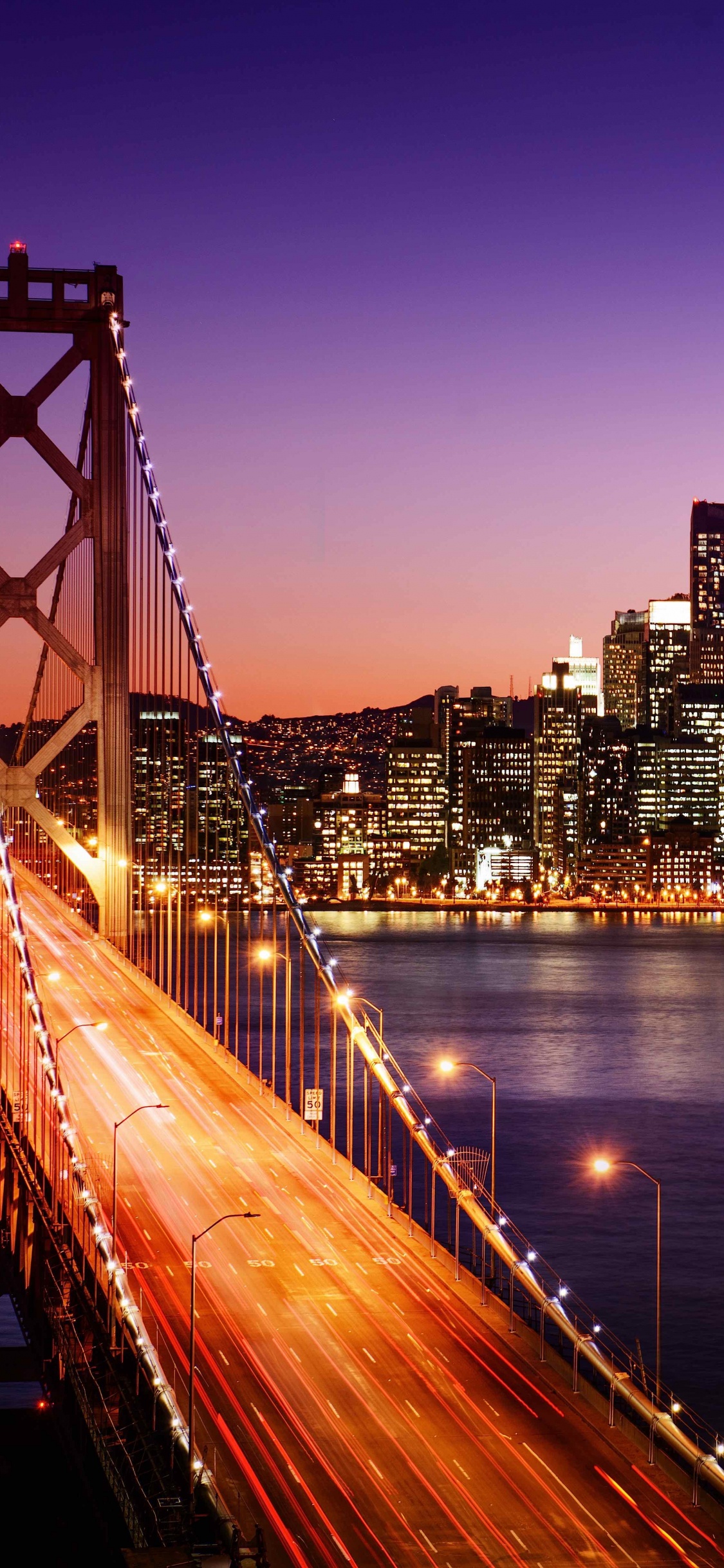 Bridge Over Water Near City Buildings During Night Time. Wallpaper in 1125x2436 Resolution